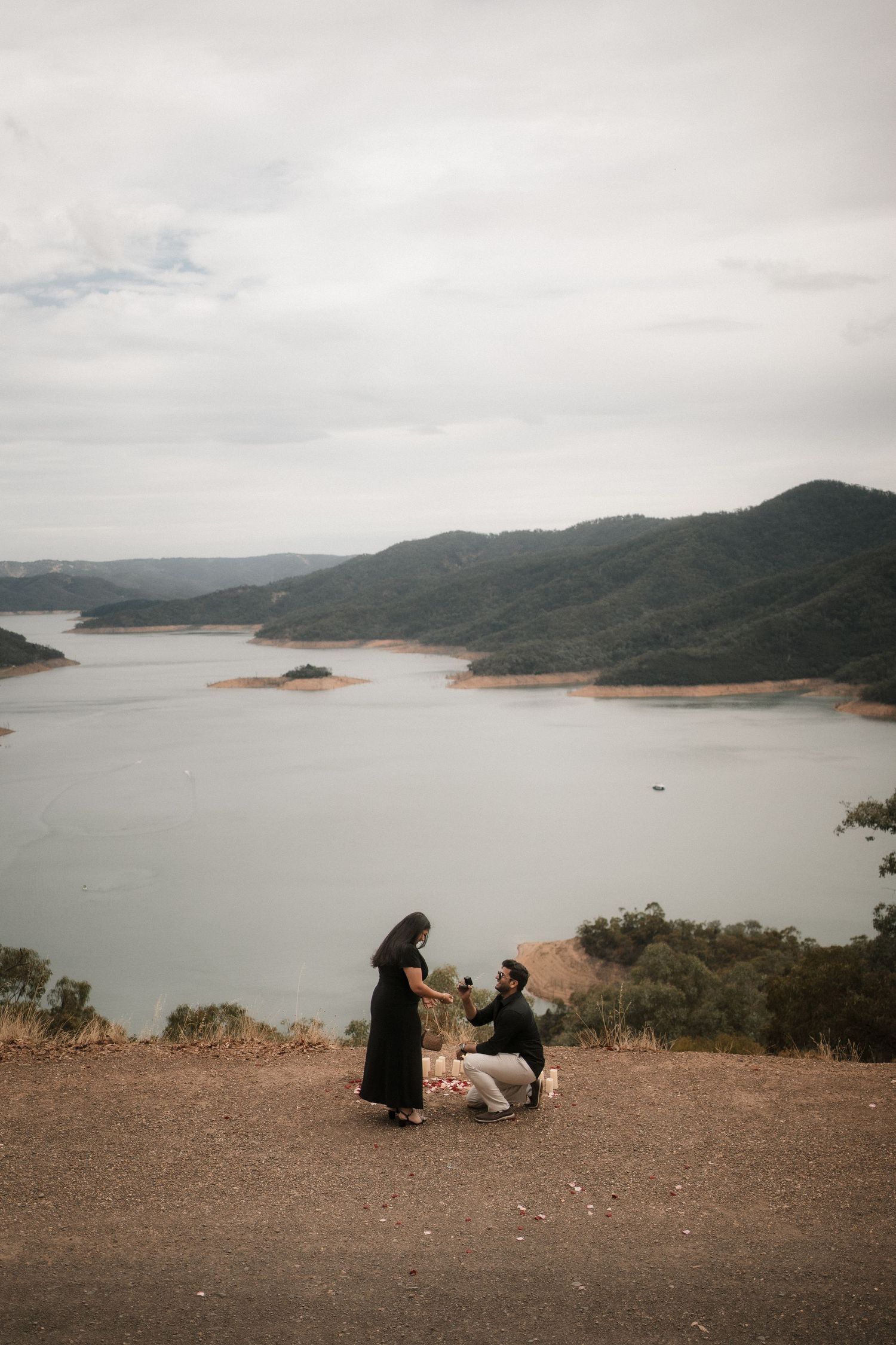 A scenic overlook of a serene lake surrounded by mountains with people sitting at the edge of a cliff.