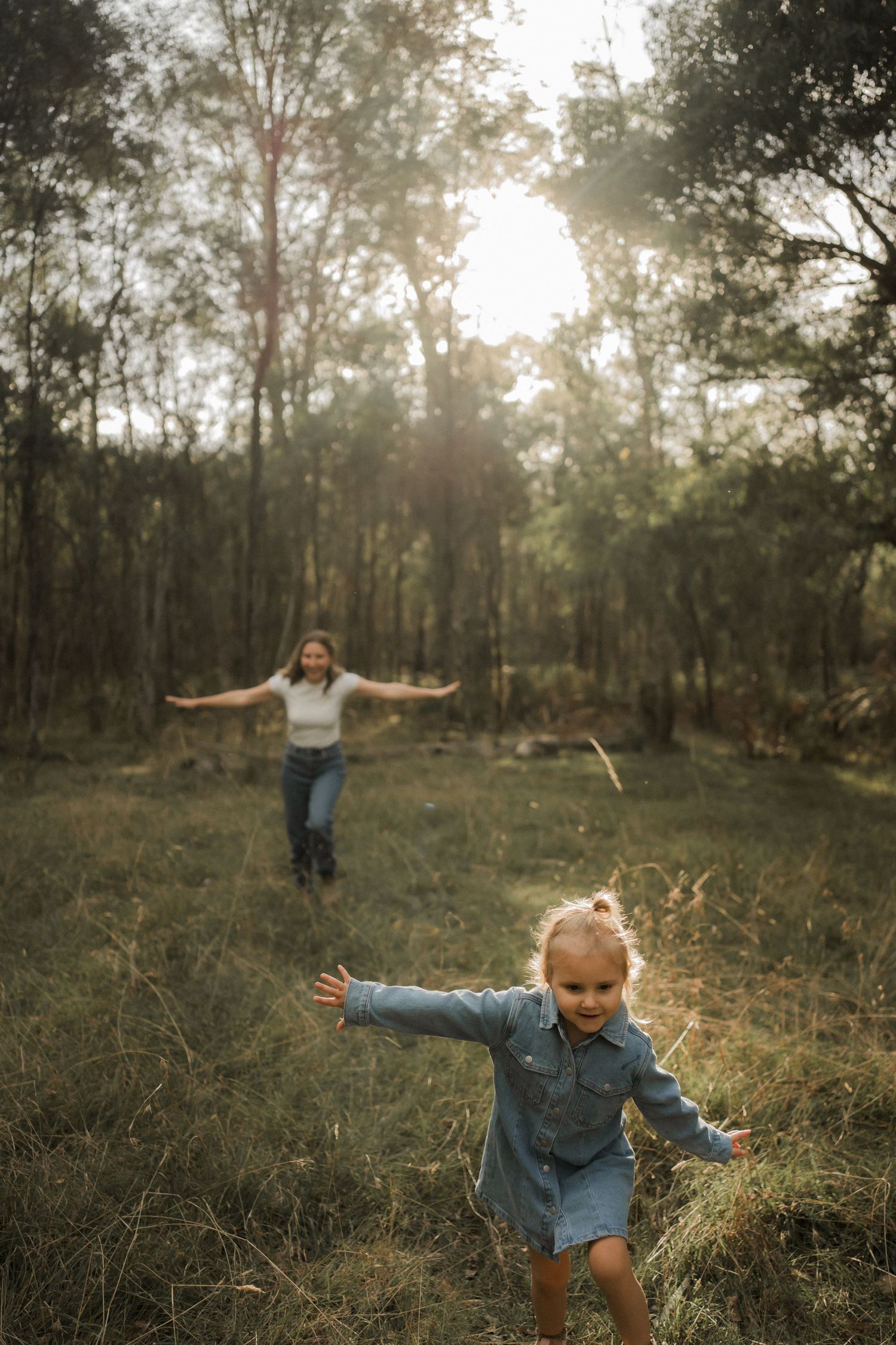 Two figures play freely in a misty forest clearing with arms outstretched in joyful movement.