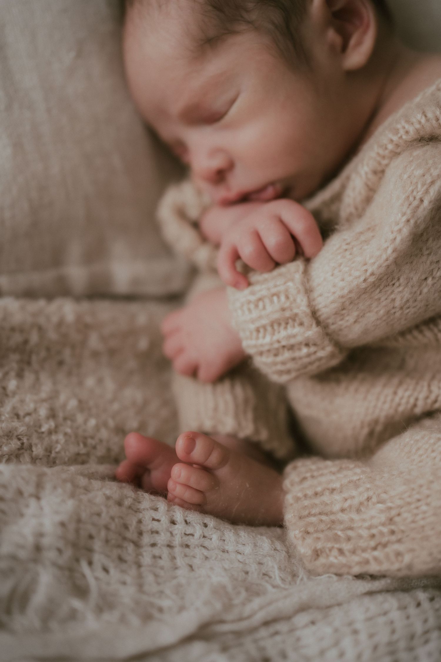 Peaceful sleeping newborn wearing cozy cream knit sweater rests on soft textured blanket.