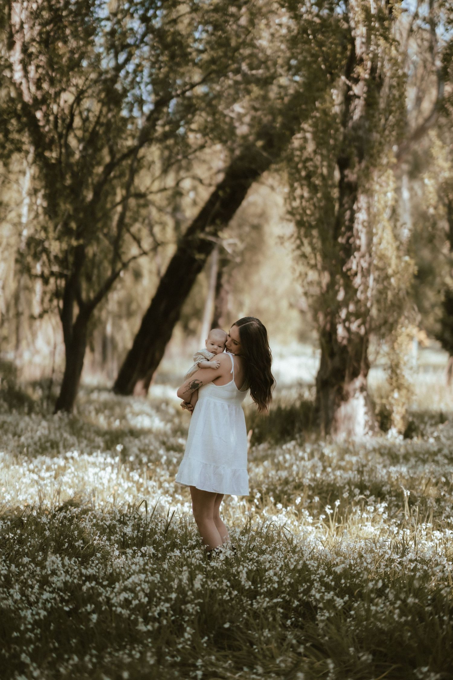 Dreamy ethereal scene of a person in a white dress standing in a sunlit forest meadow with wildflowers.