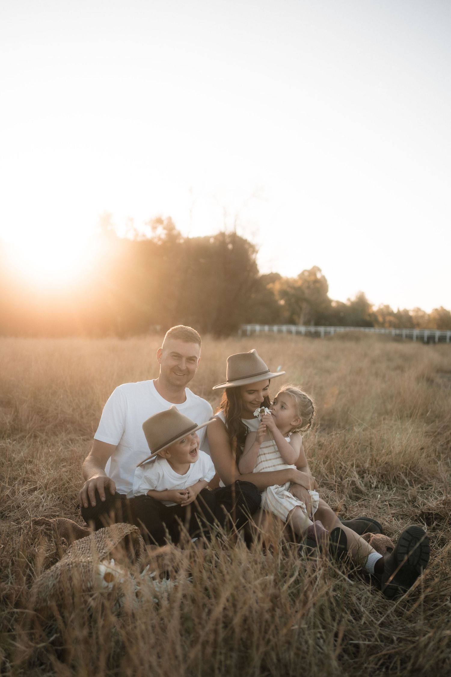 A couple shares an intimate moment while laying in a sun-drenched field of tall grass at sunset.
