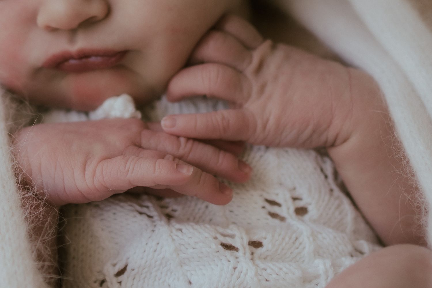 Small hands grip the edge of a delicate white lace blanket in soft, natural lighting.