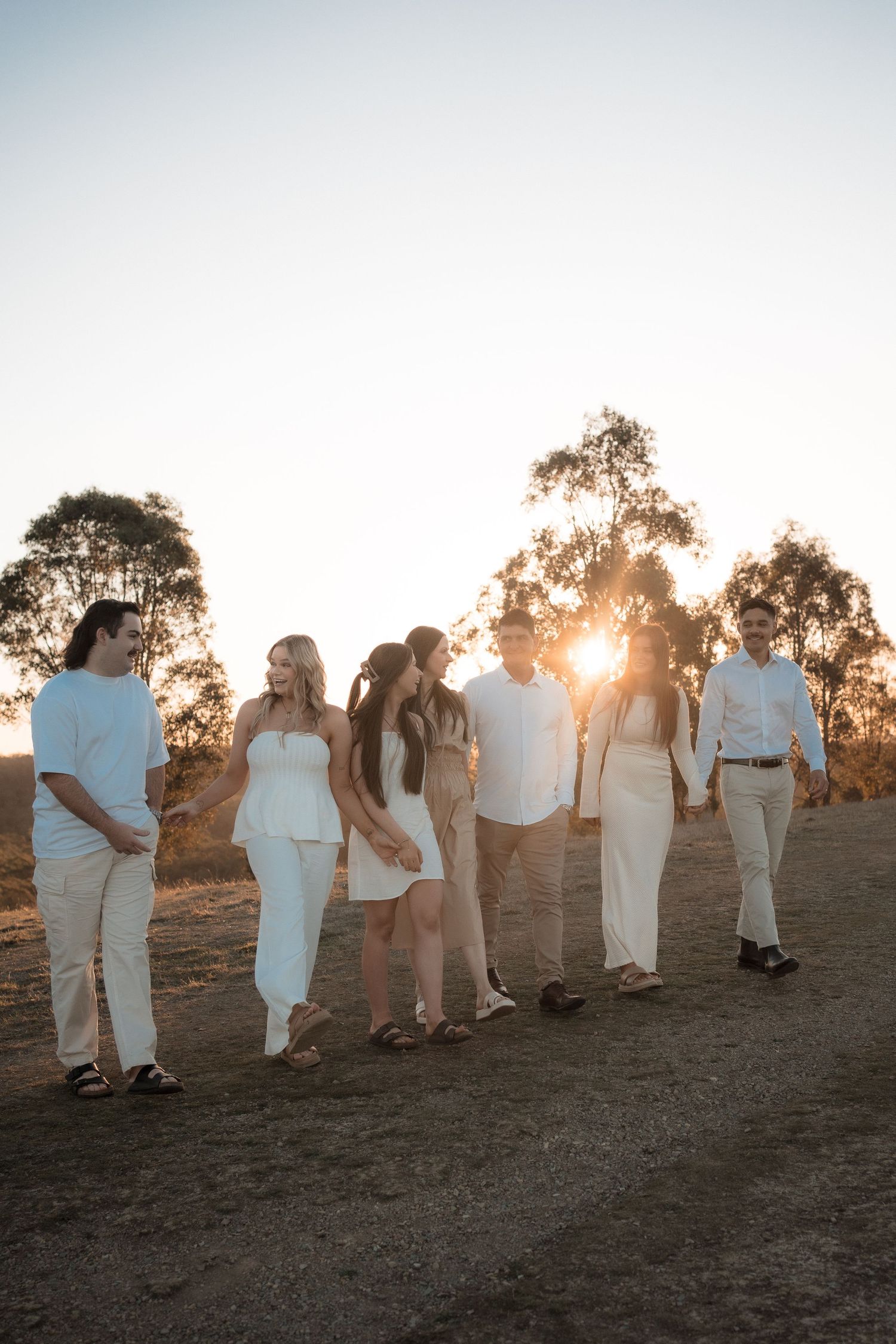 A group stands together outdoors at sunset wearing light colored clothing against a backdrop of eucalyptus trees.