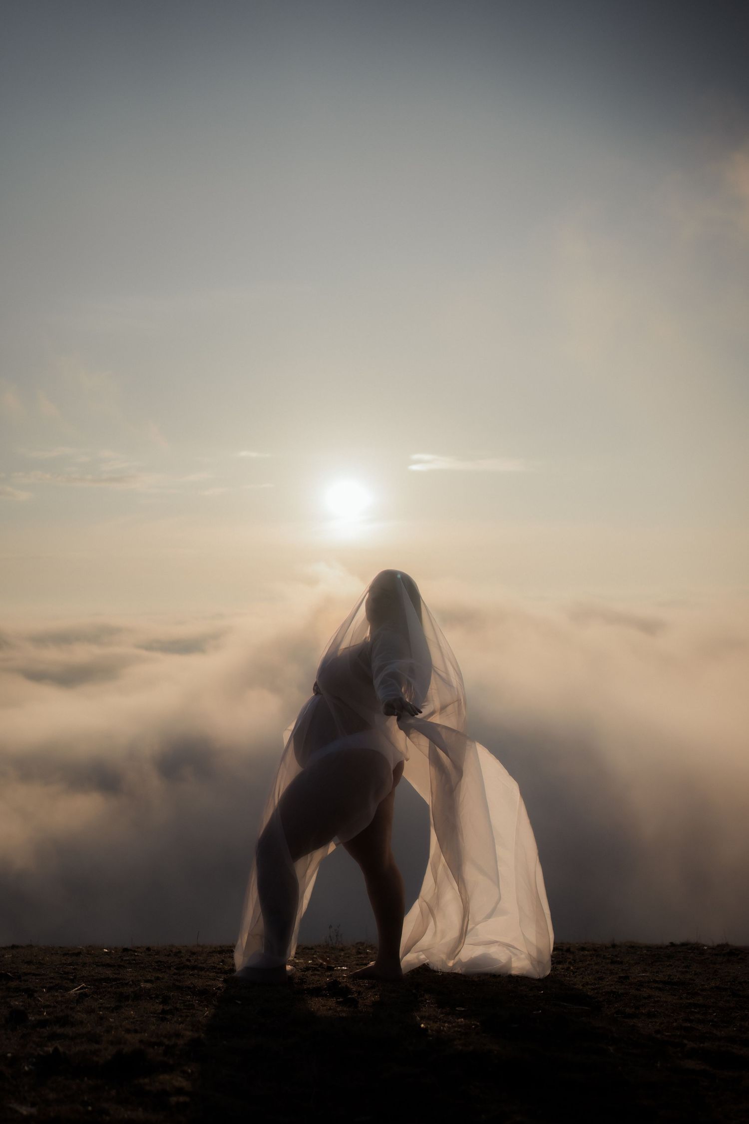 Dramatic silhouette of pregnant figure against sunset sky and fog.