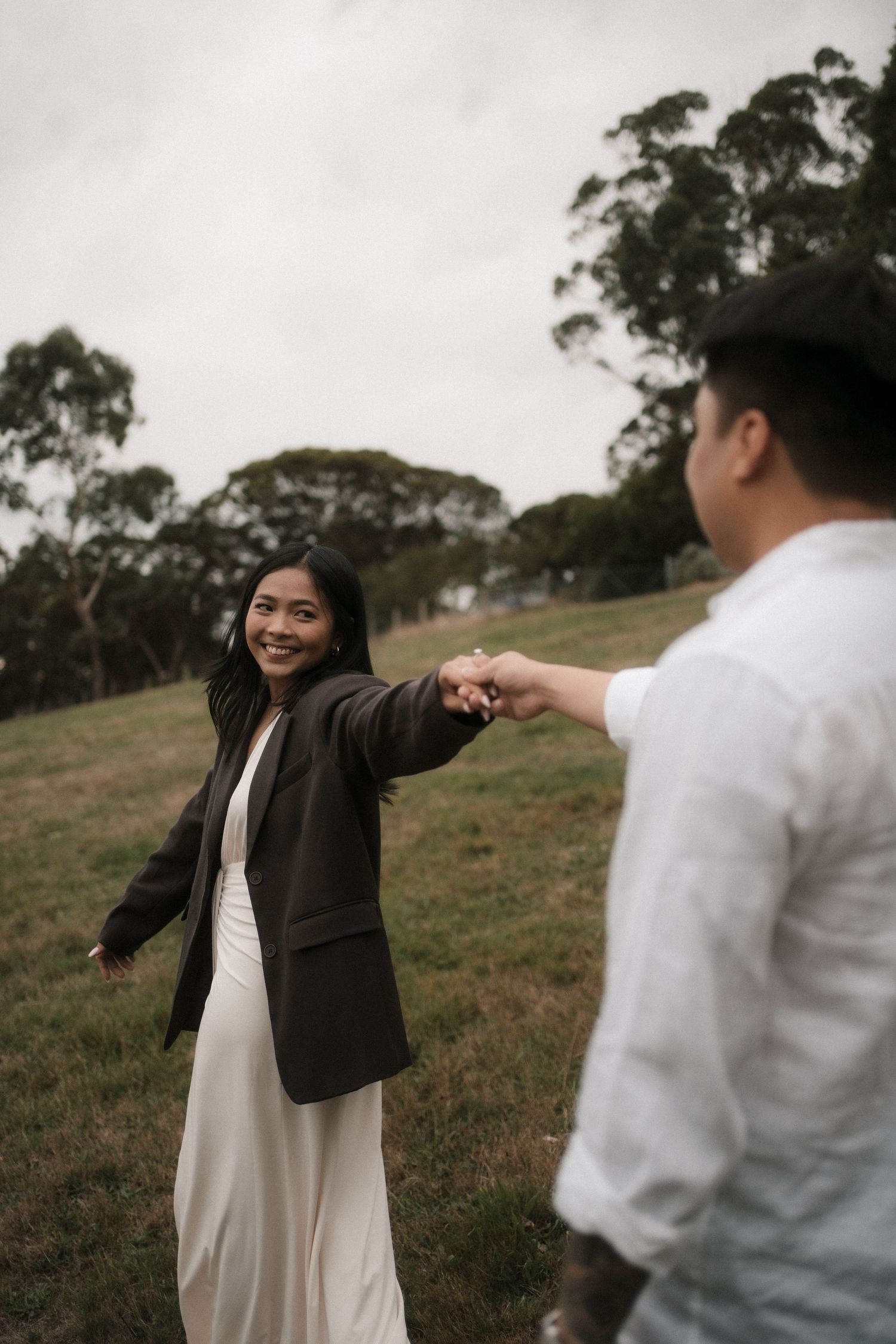 A couple shares a playful moment in a grassy field during a photo session at sunset.