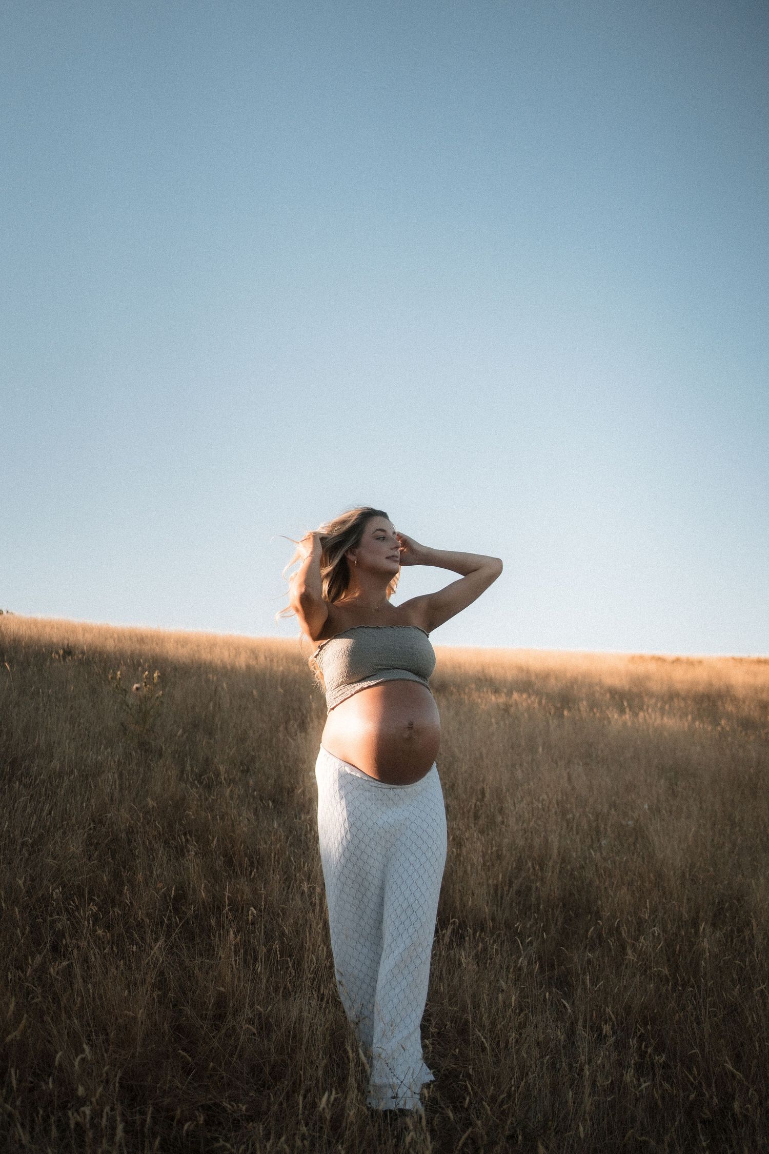 A figure in a white dress stands gracefully in a golden field at sunset, creating a dreamy silhouette against the sky.