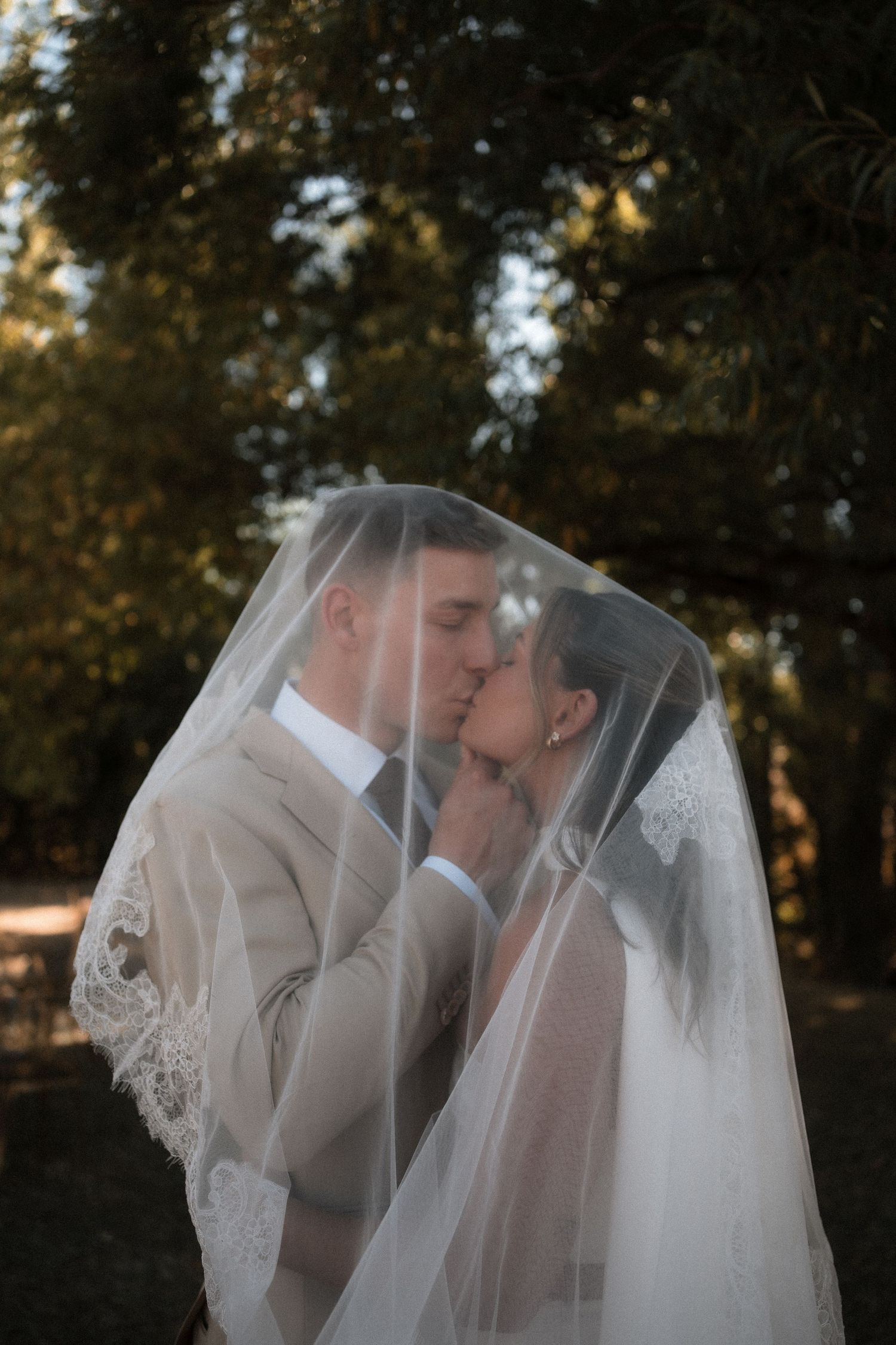 A romantic wedding moment captured outdoors with a long lace veil and soft autumn lighting in the background.
