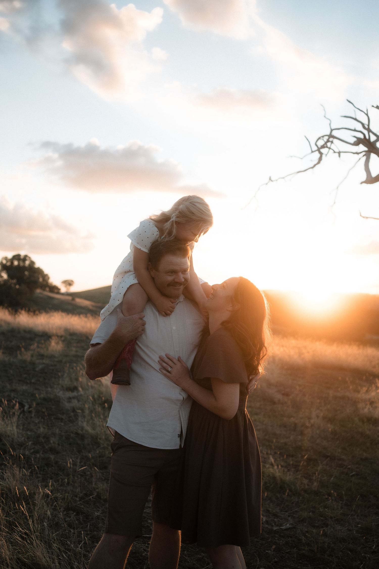 A couple embraces playfully in a golden sunset field, creating silhouettes against the warm evening sky.