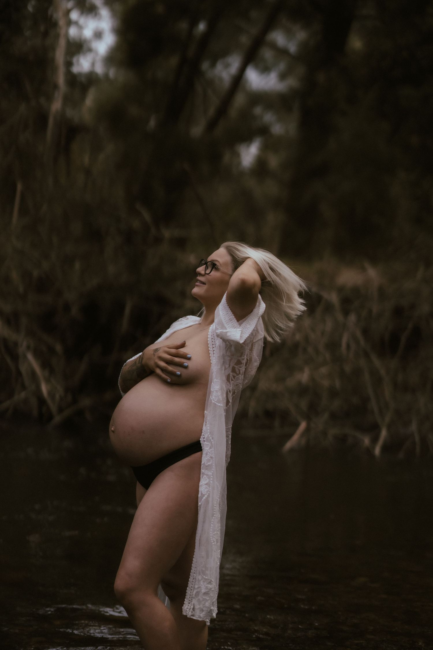 An artistic maternity photo captured in dark moody lighting near water.