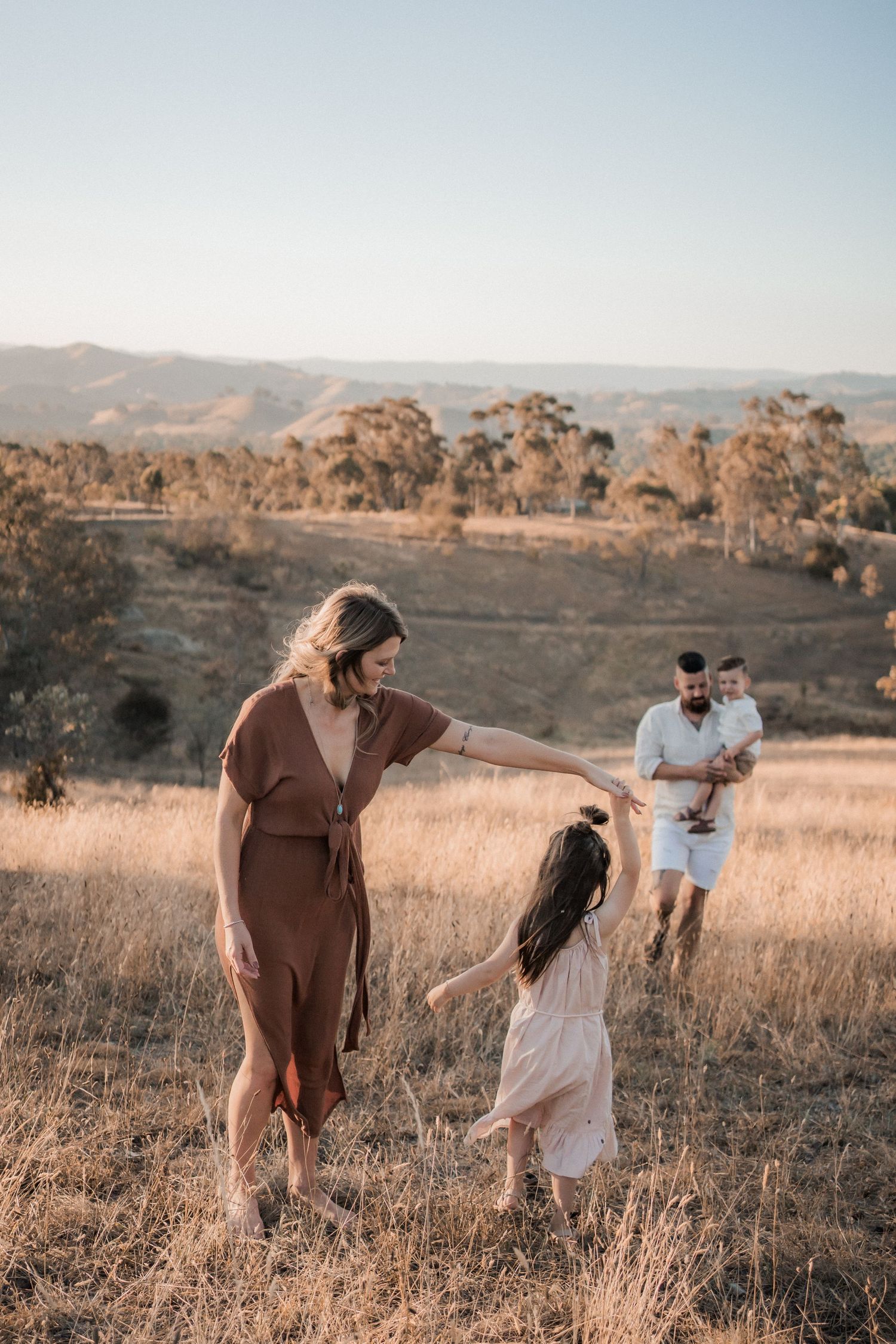 Family enjoying a sunset moment together in a golden field with rolling hills and eucalyptus trees in the background.