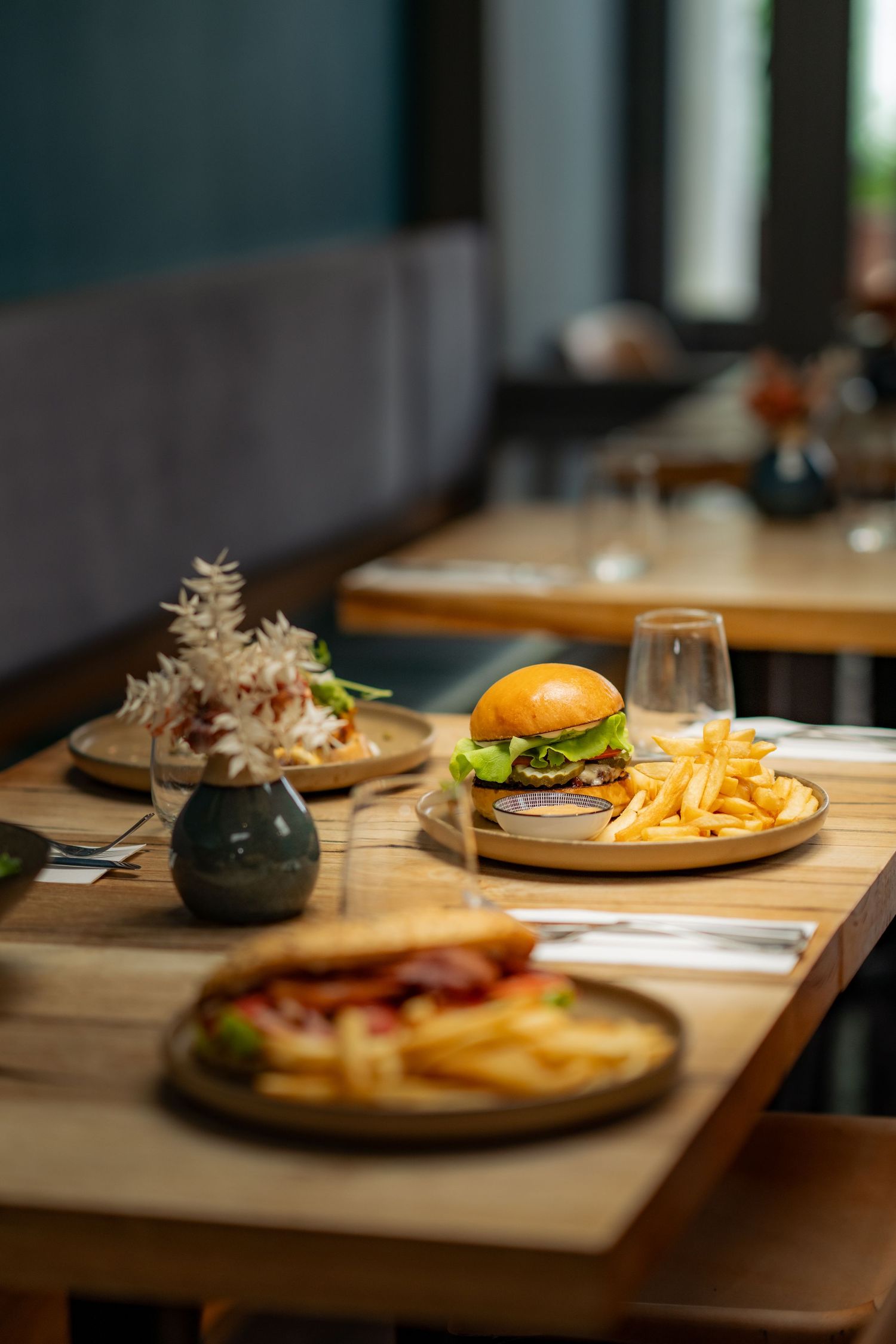 Close-up of gourmet burger and french fries served on wooden plates at a restaurant table with ambient lighting.