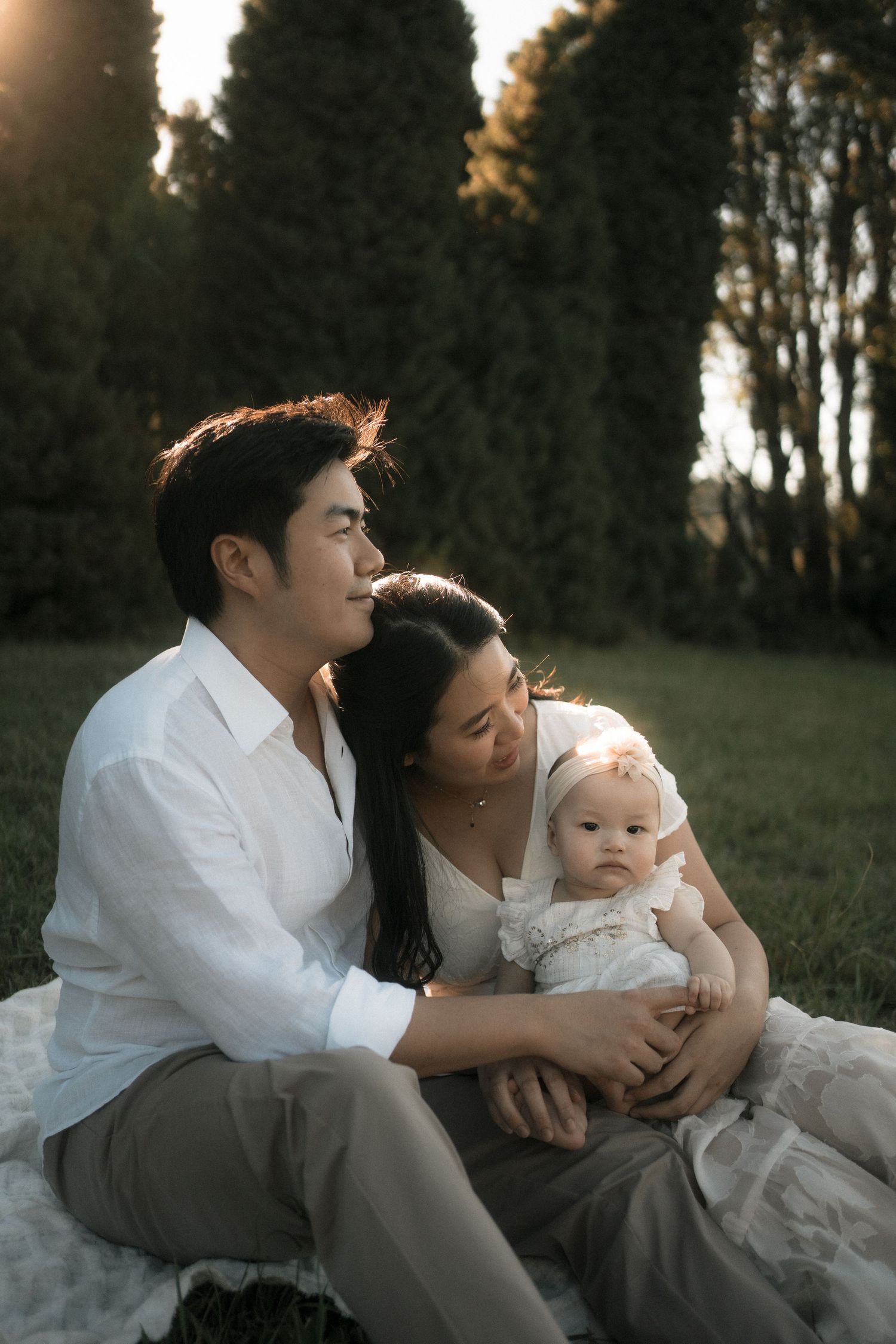 A family sits together on a blanket outdoors during golden hour, sharing a tender moment in nature.
