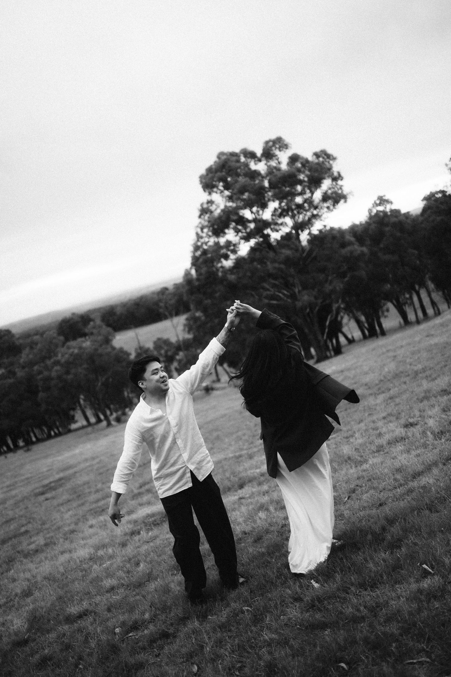 A couple in black and white attire dances playfully across a grassy hillside in a candid sequence of photos.