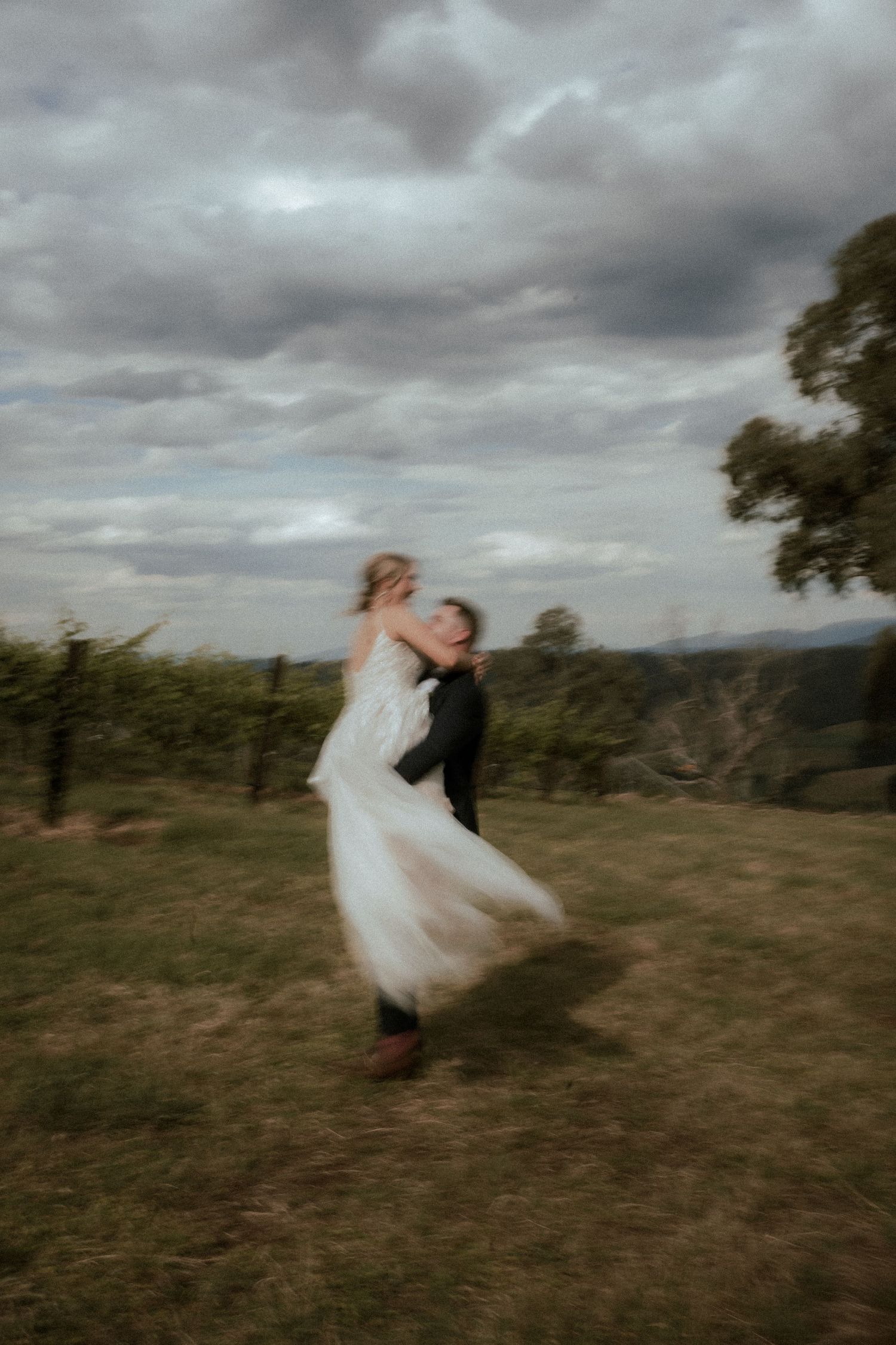 Dancing newlyweds twirl on hilltop under dramatic cloudy sky.