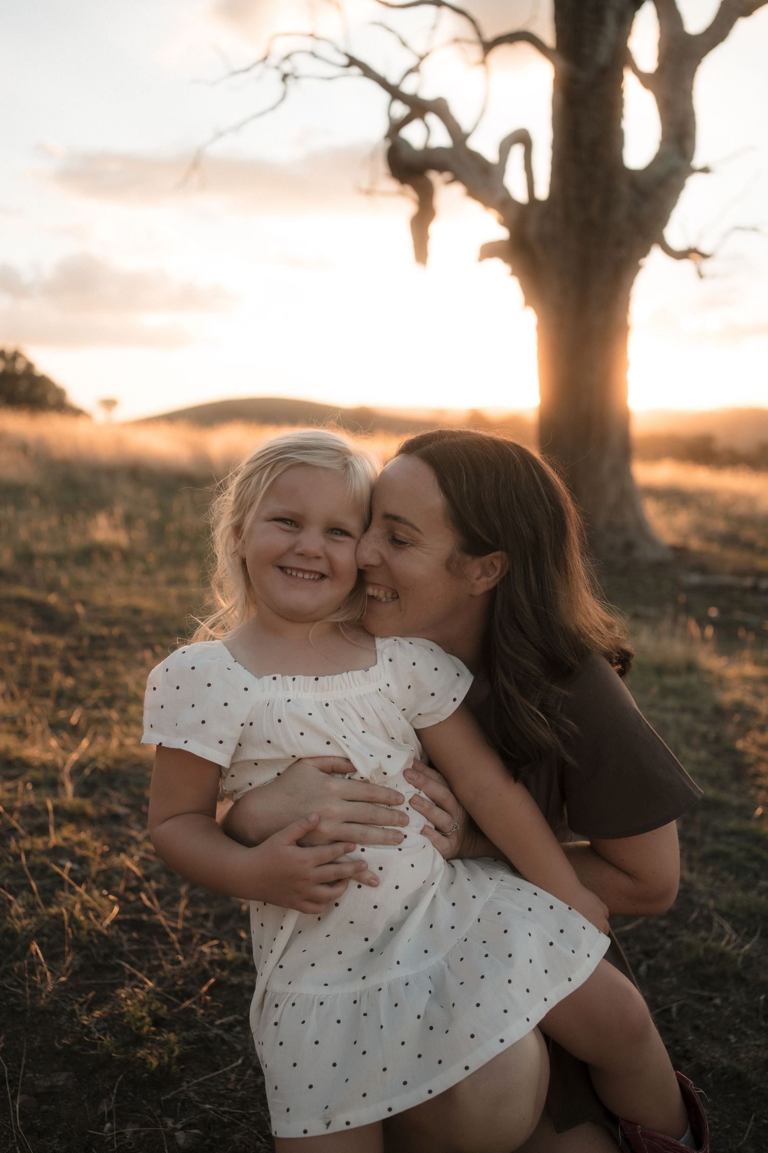 A tender moment between parent and child sitting together outdoors during golden hour sunset.