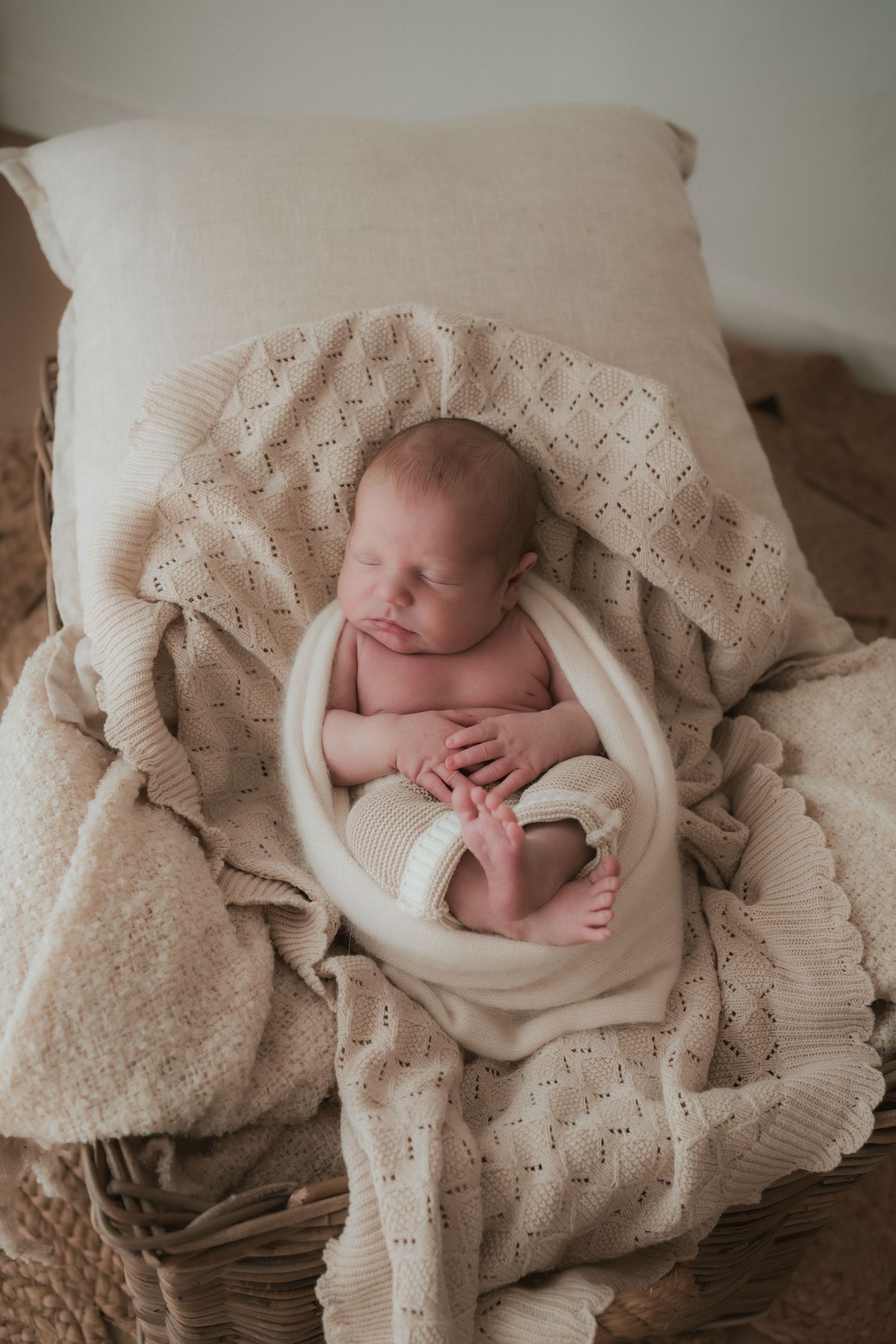 Peaceful newborn baby sleeping in soft knitted blanket on beige pillow during professional photo session.