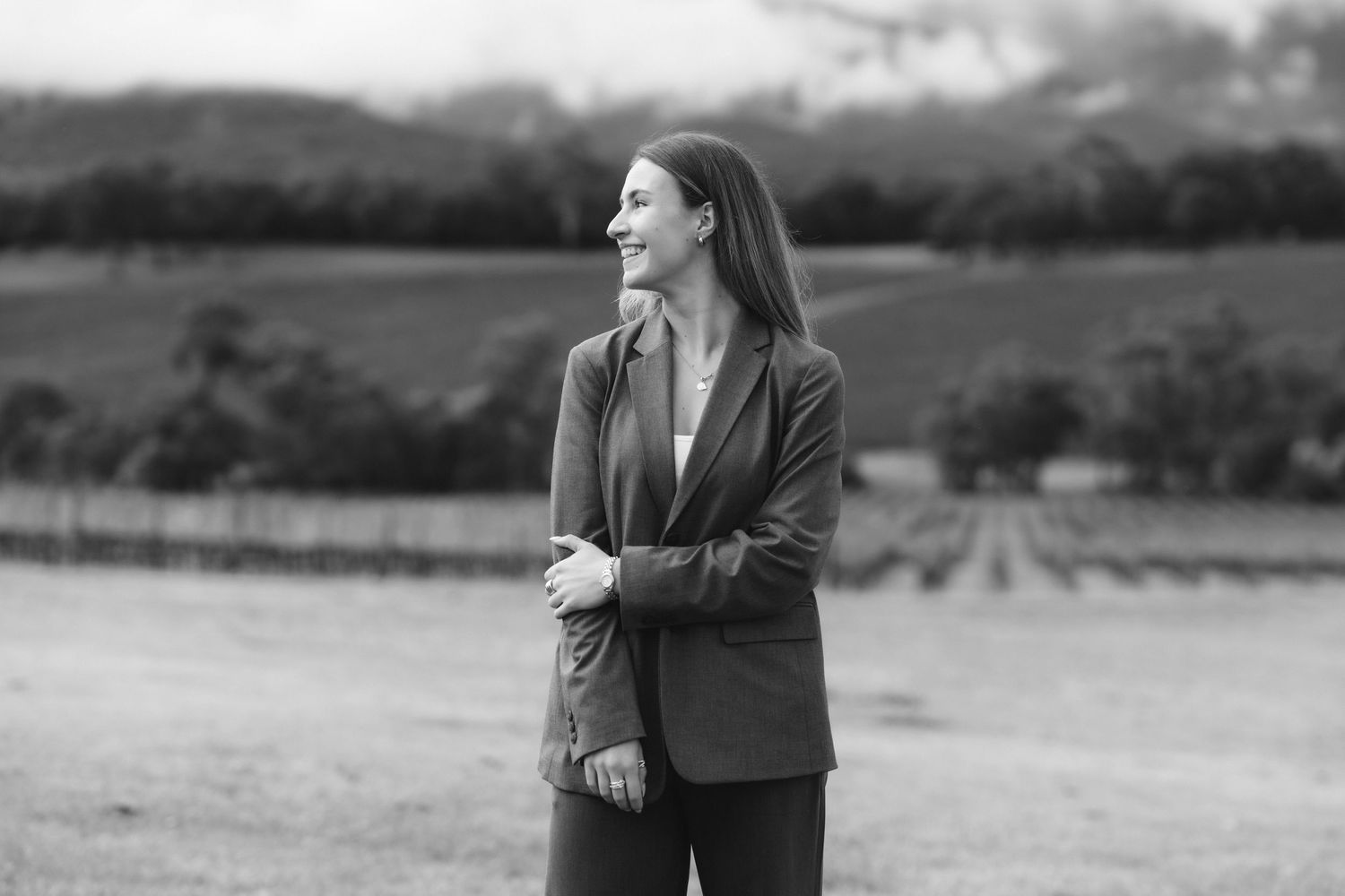 A couple shares a romantic moment in a vineyard setting at sunset with rolling hills in the background.