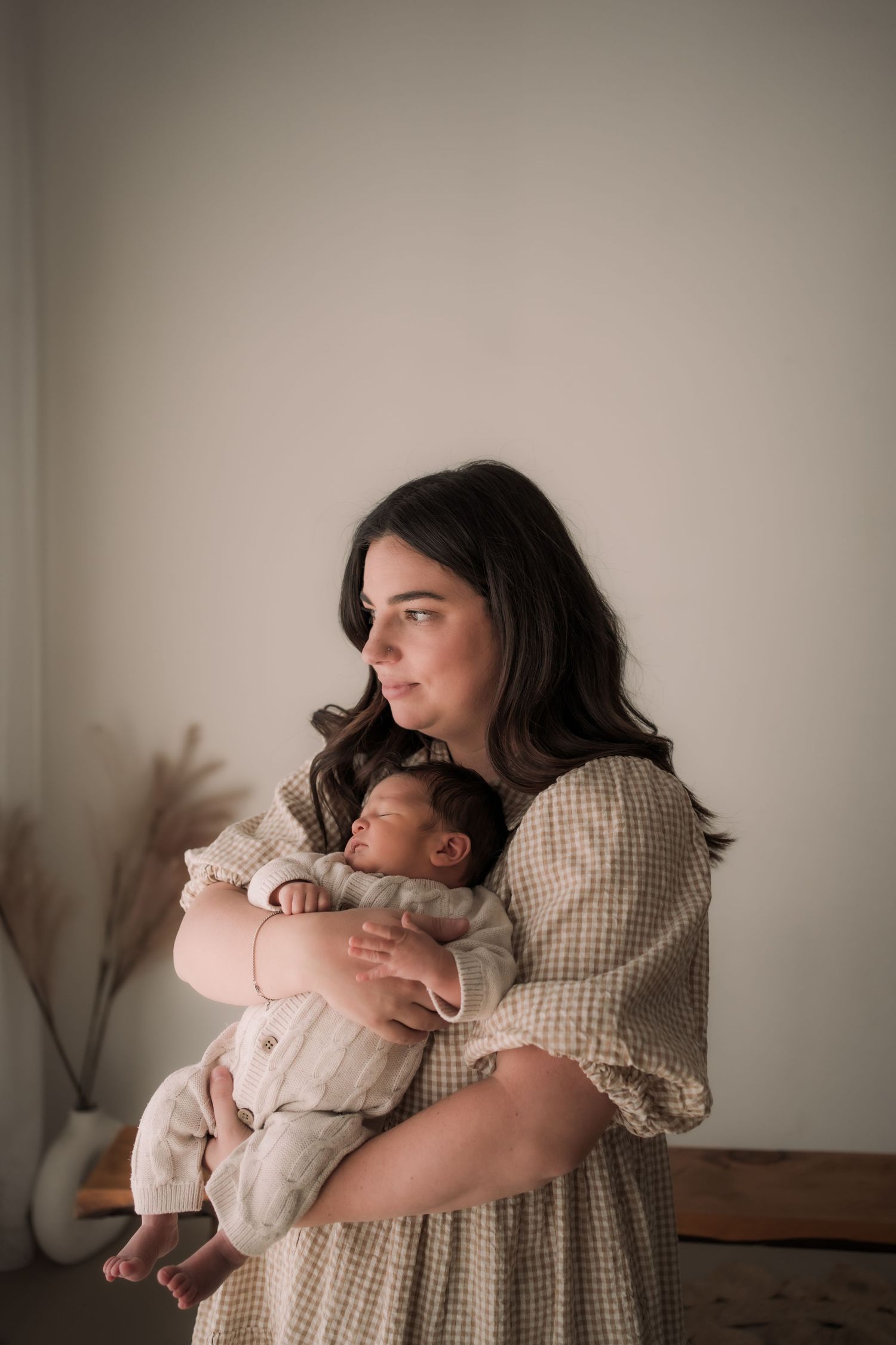 A series of tender maternal moments captured in warm, muted tones as a mother embraces her baby against a neutral backdrop.