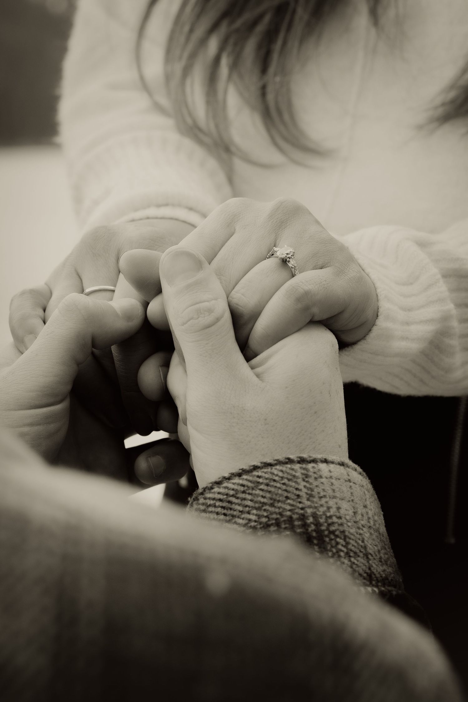 Close-up black and white photo of engaged couple holding hands with ring.