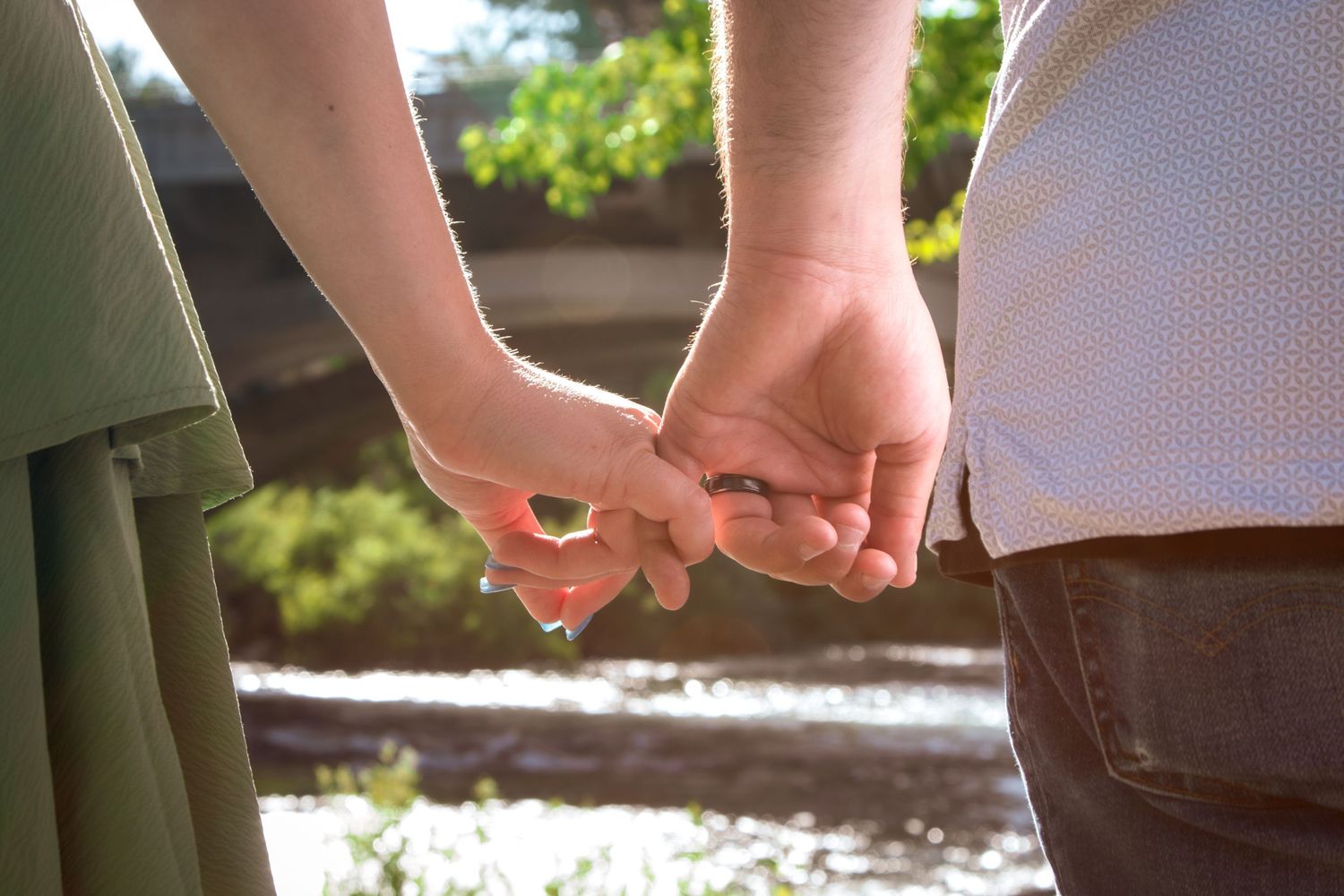 Close-up of a couple holding hands outdoors in warm sunlight, symbolizing love and connection.
