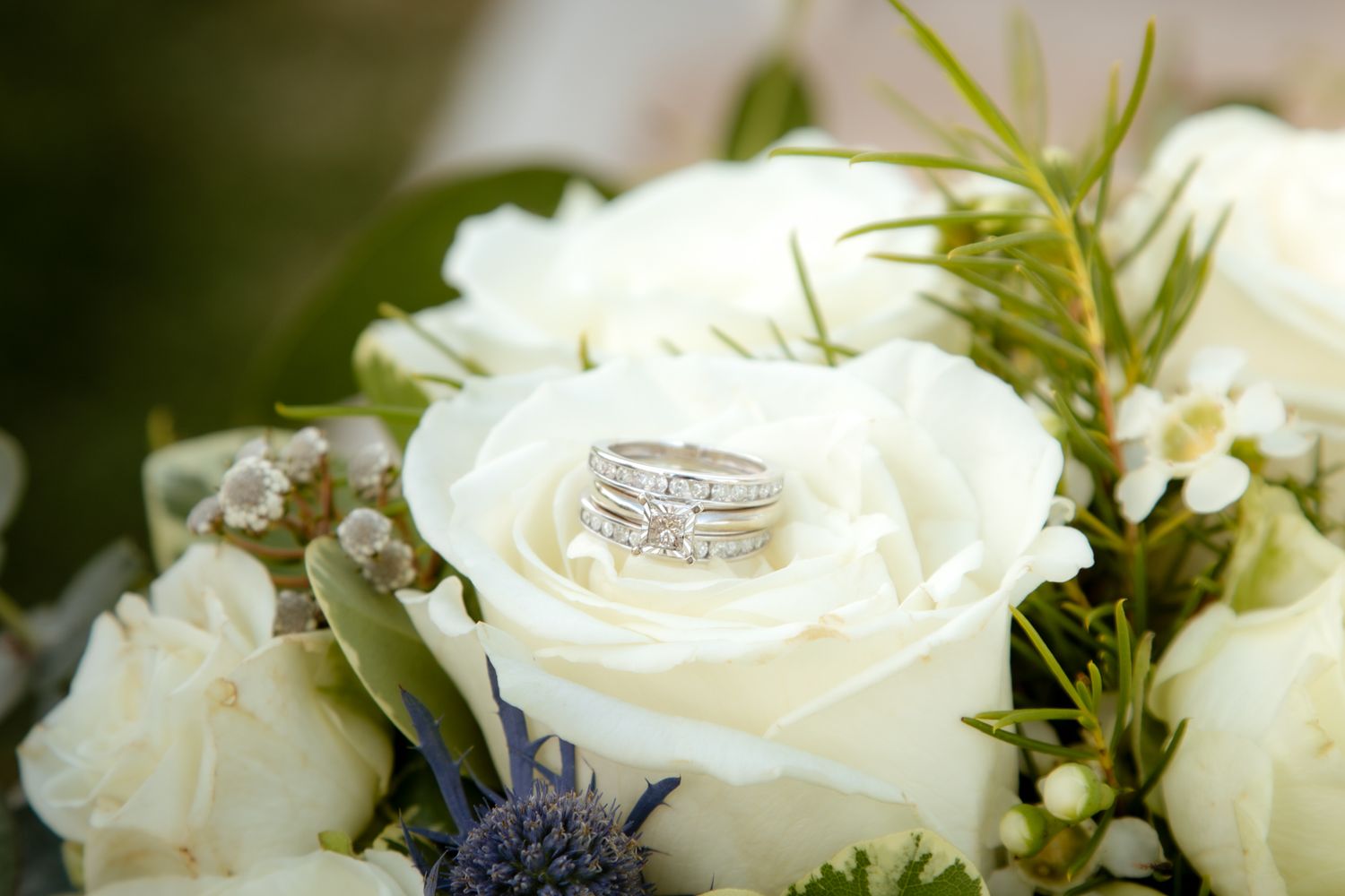 Diamond wedding and engagement rings rest elegantly on white roses in a bridal bouquet.