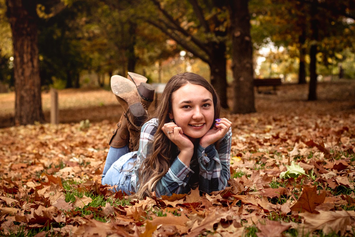 Young woman lying in autumn leaves in a park, smiling at camera during fall season outdoor portrait.