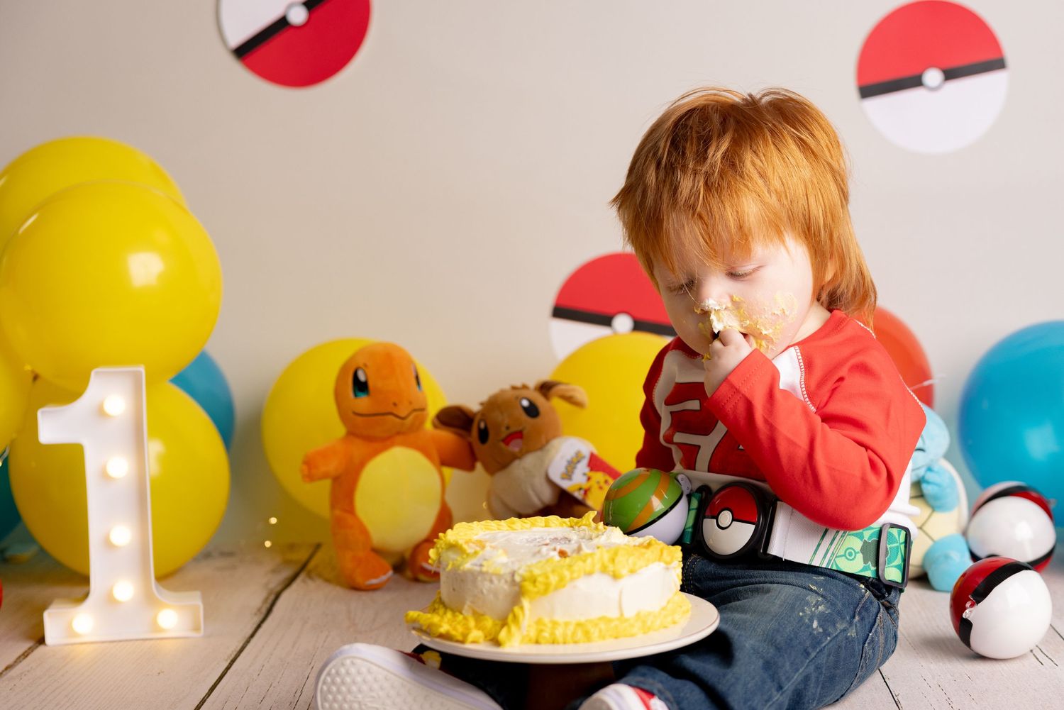 Pokemon themed birthday party decorations with colorful balloons, Pokeball props, and a yellow frosted cake on display.