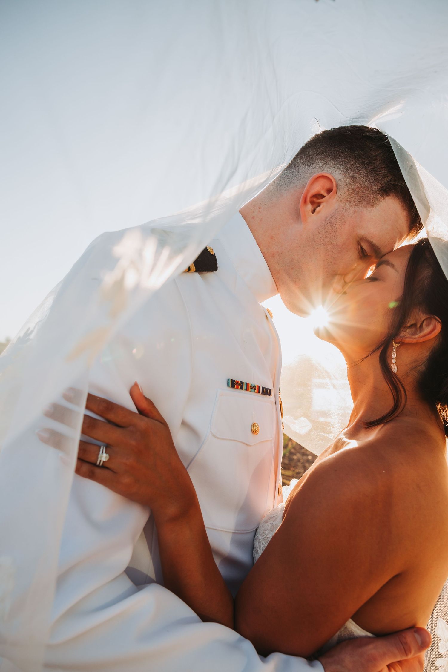 Intimate close-up shots of couple embracing under white sheets with sunlight streaming through fabric.