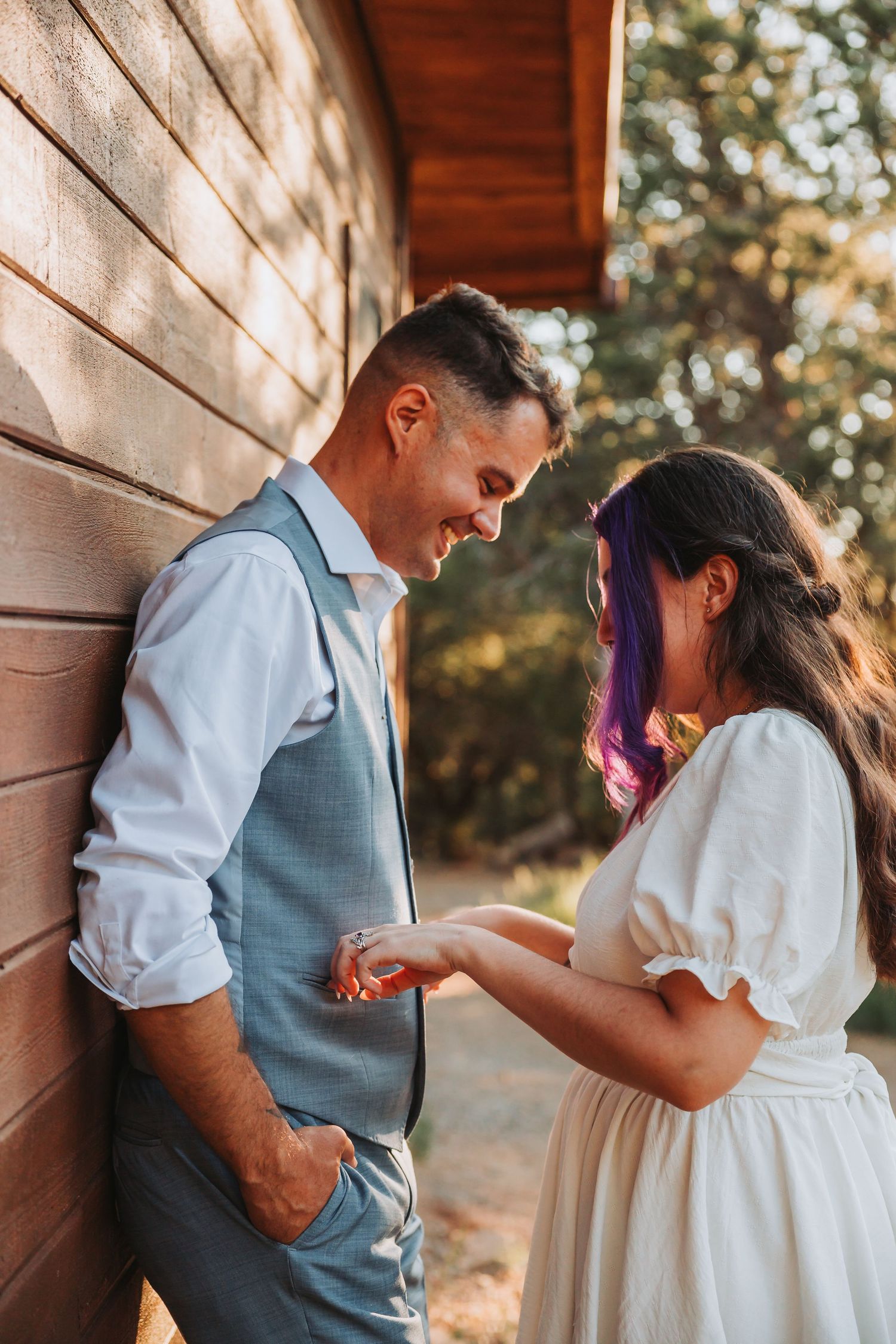 A couple shares a tender moment together against a rustic wooden wall in soft natural lighting.