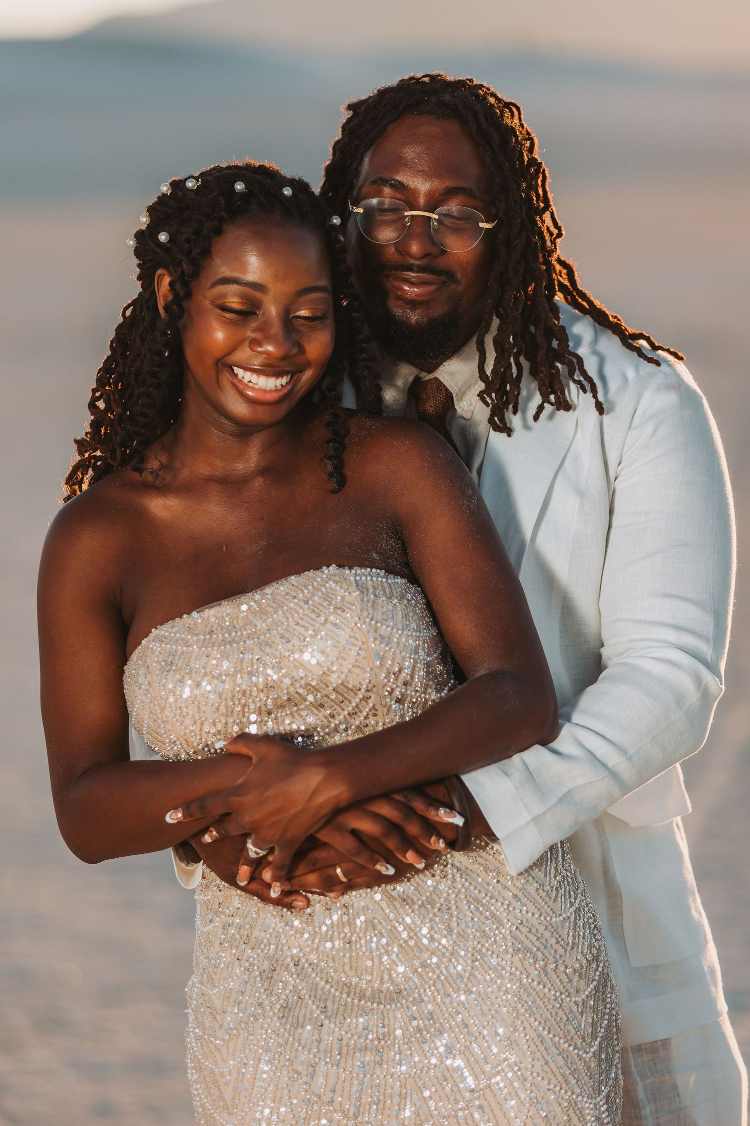 A couple shares intimate moments on the beach at sunset in a white wedding dress and suit.