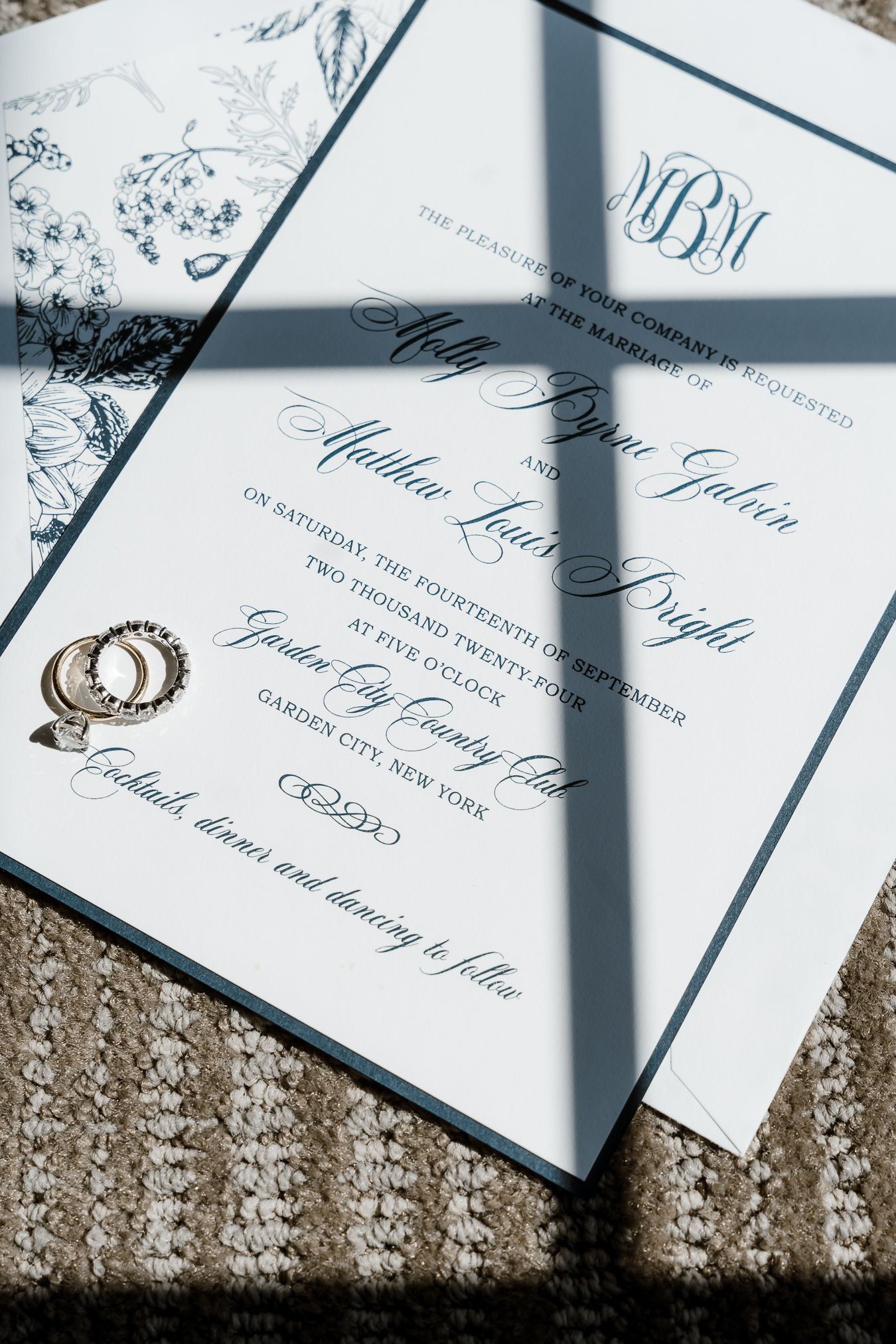 Elegant white wedding invitations with navy blue calligraphy text arranged in a row on a textured surface.
