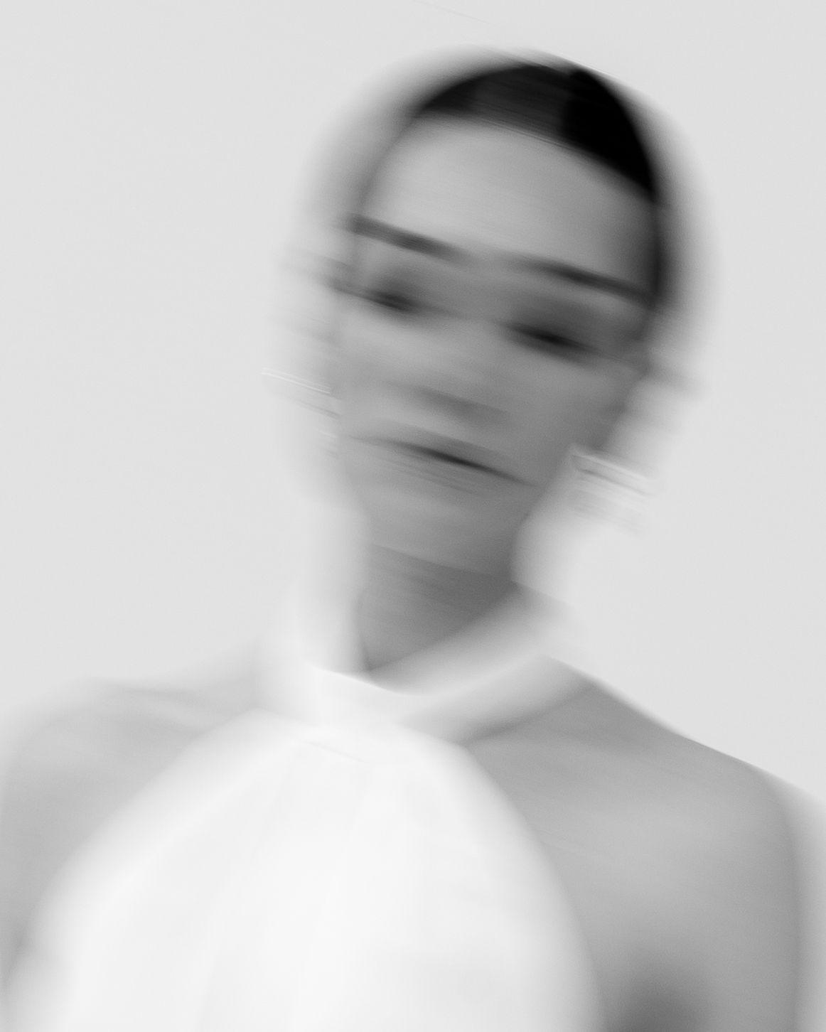 Black and white blurred portrait of a woman in a white halter top, artistic motion blur effect.
