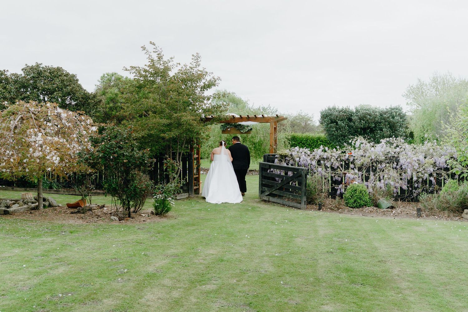 Panoramic view of a spring garden wedding ceremony setup with white chairs and blooming trees in the background.