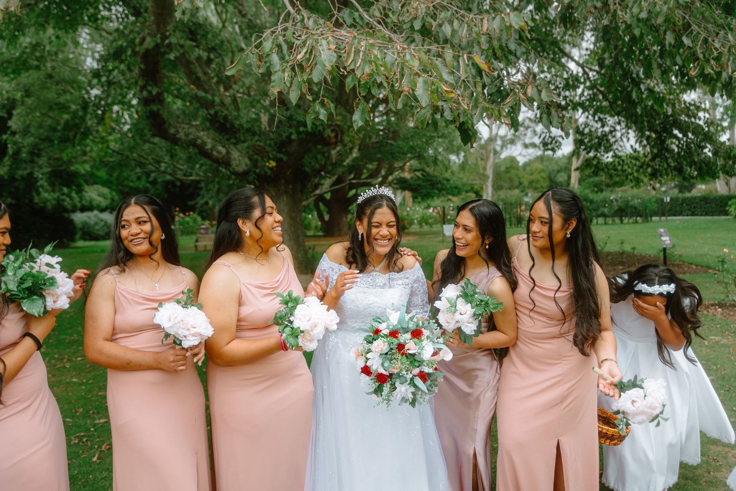 Bridesmaids in blush pink dresses and the bride in white share joyful moments together in a lush garden setting.