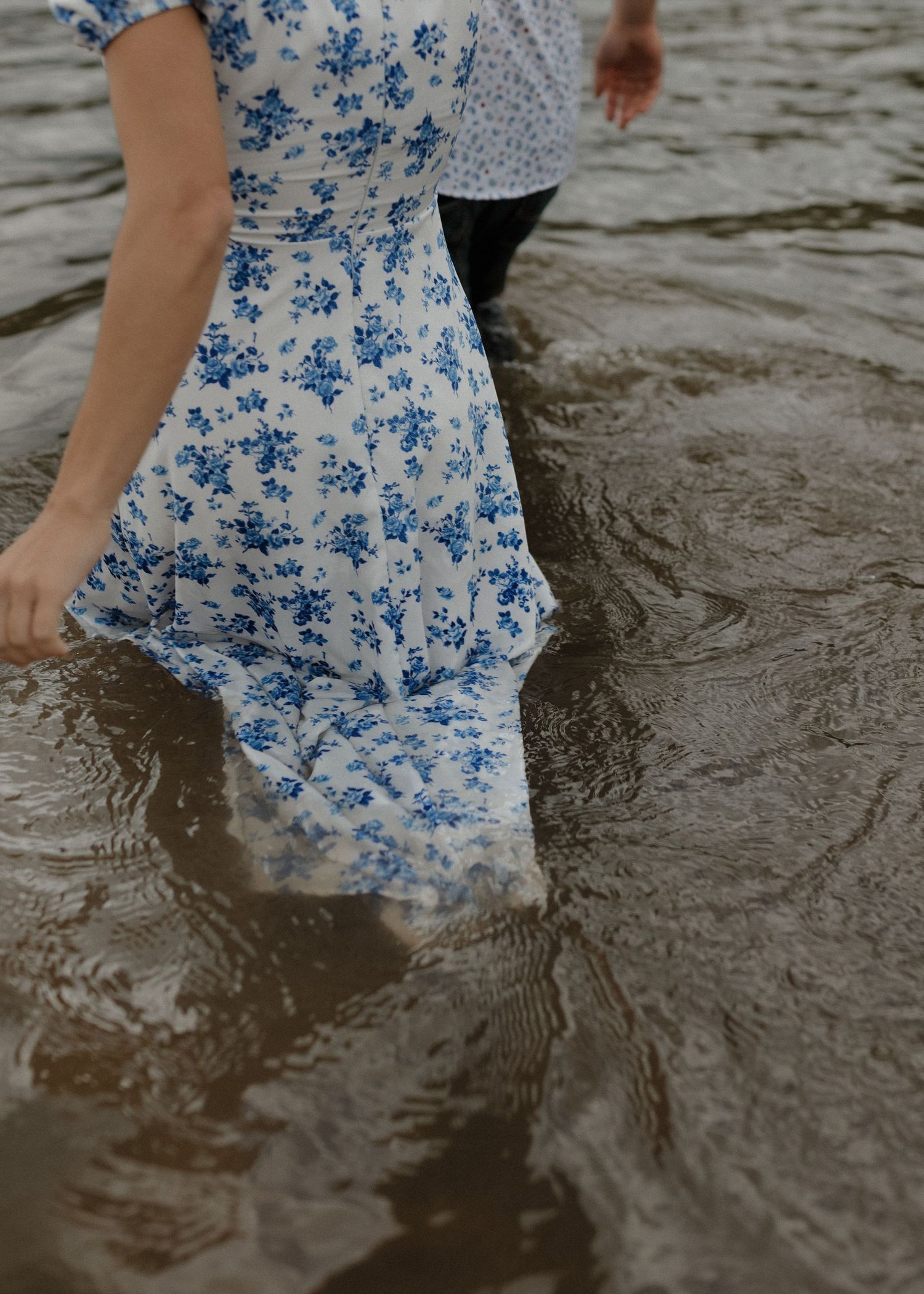 Person wearing a blue and white floral dress walks through rippling water creating reflective patterns.