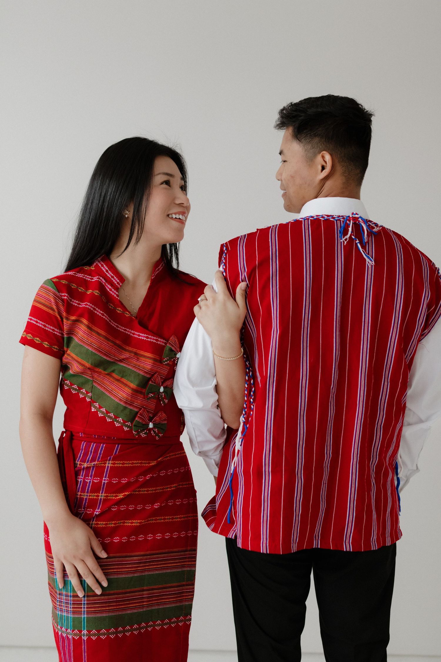 A couple wearing traditional red striped attire pose together against a white backdrop.