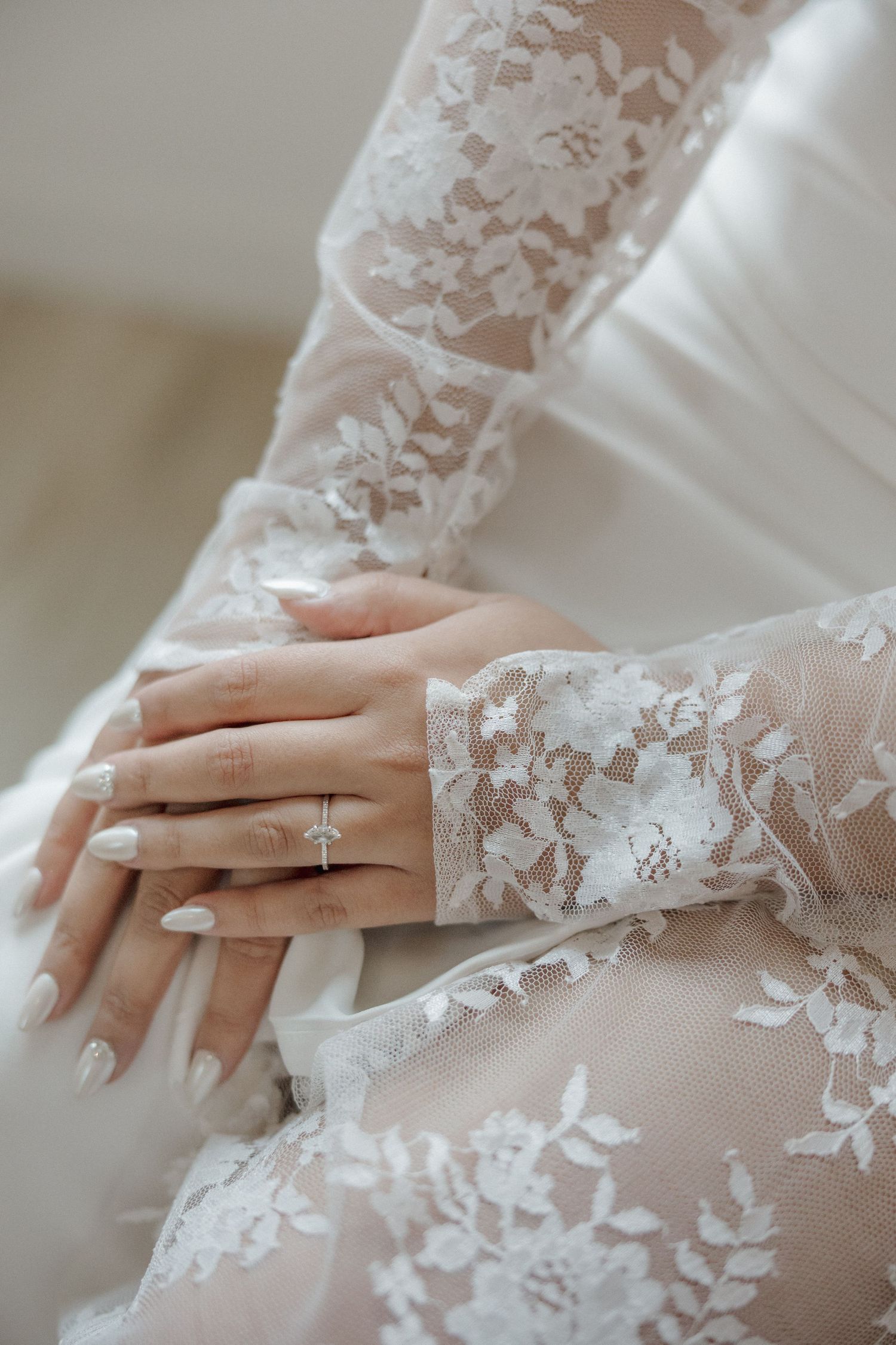 Delicate white lace sleeve detail of a wedding dress with elegant engagement ring and manicured nails.