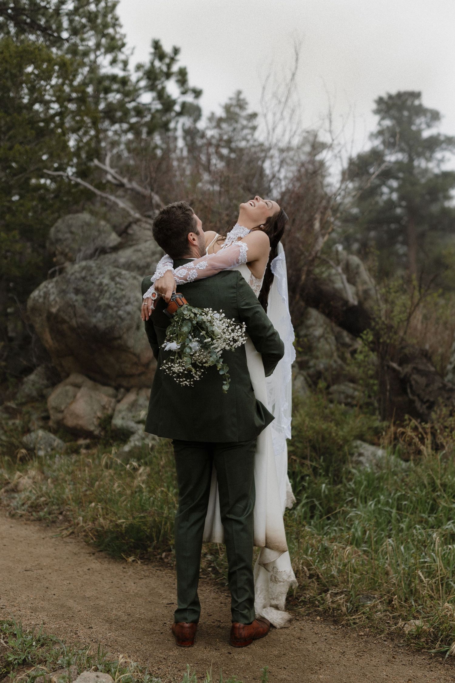 A couple embraces on a rocky trail surrounded by nature during an intimate outdoor wedding ceremony.