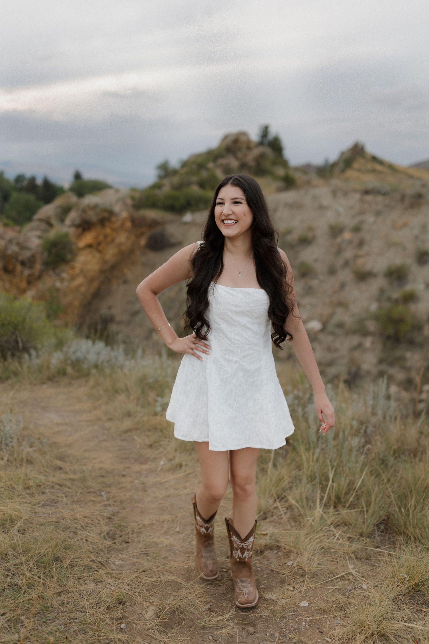 A child in a white dress and brown boots runs playfully through a rocky desert landscape.