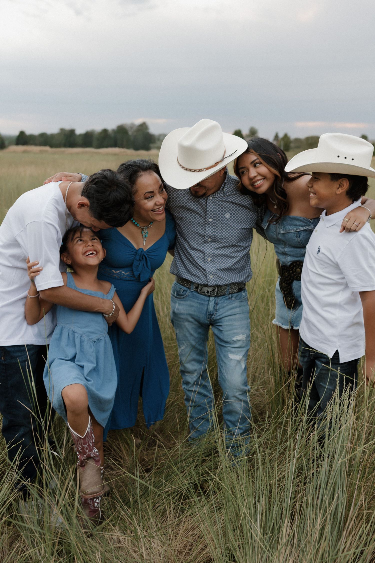 A group of friends casually pose together in a grassy outdoor field wearing casual denim and white clothing.