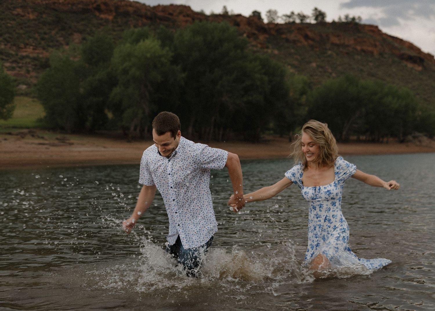A couple splashes and plays together in a lake at sunset creating joyful moments in nature.
