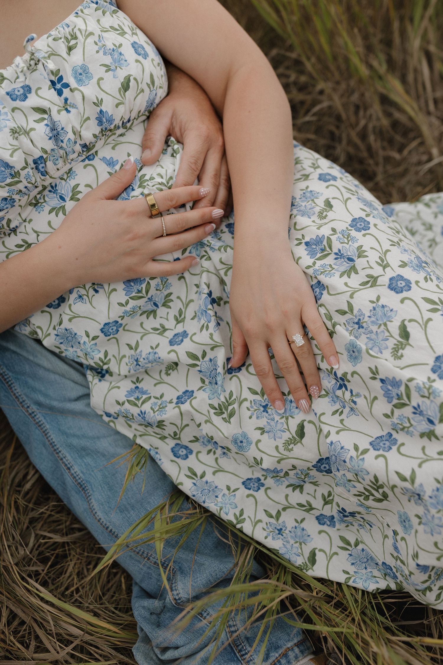 Close-up shots of hands resting on a floral dress and jeans while sitting in grass and wildflowers.