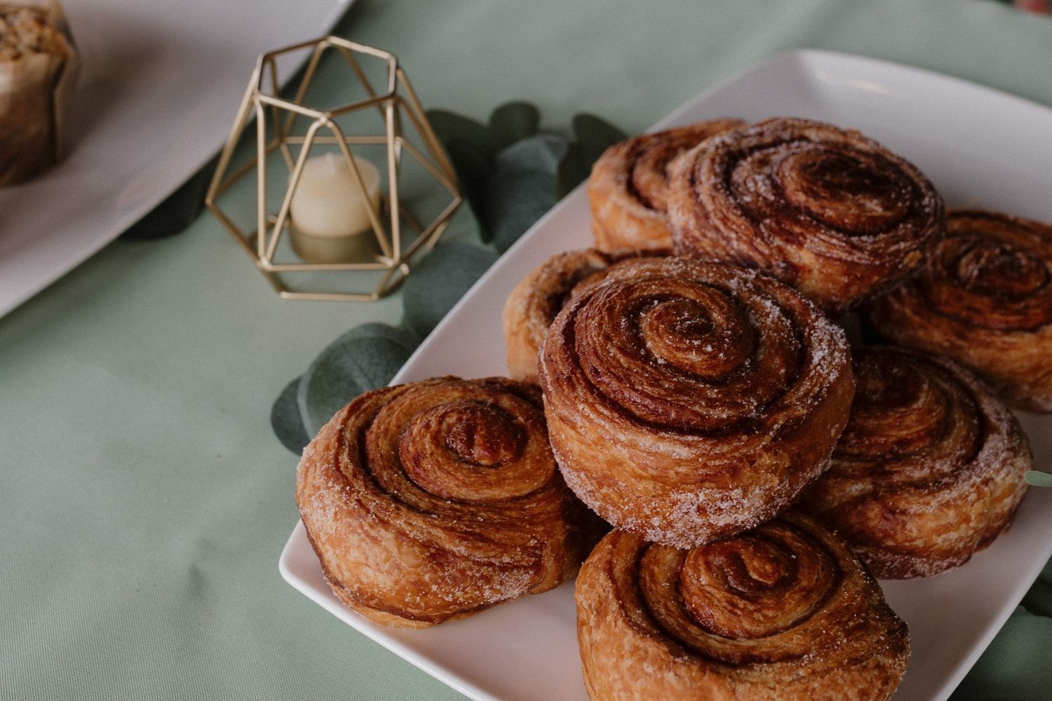 Freshly baked cinnamon rolls on a white plate with a decorative gold geometric candle holder in the background.