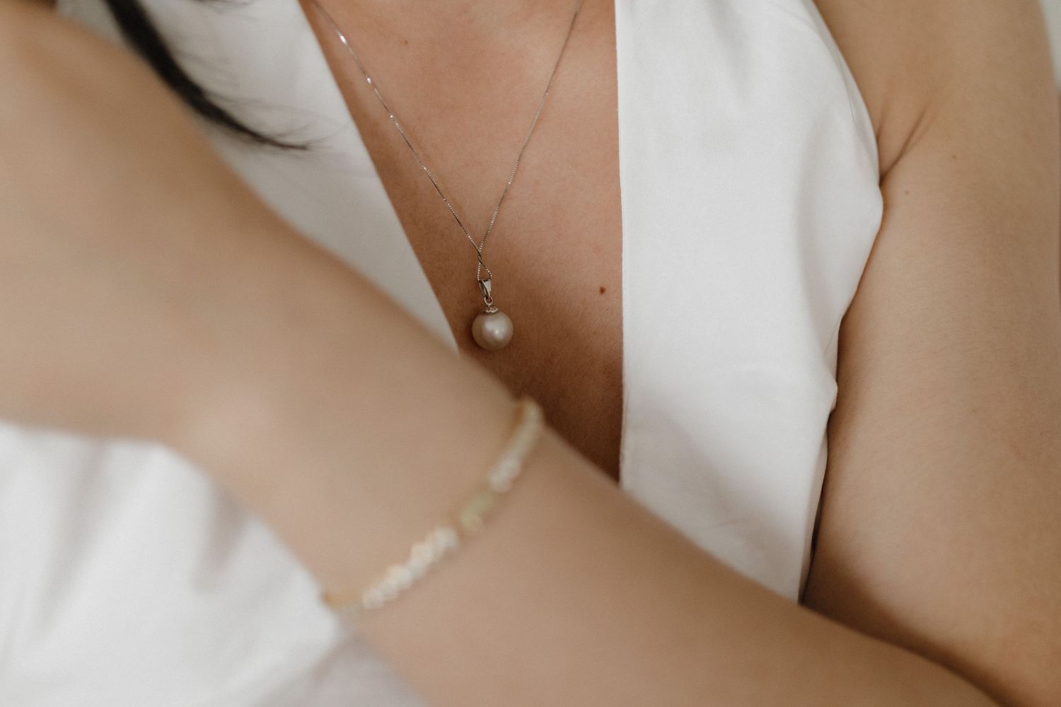 Close-up view of a delicate pearl pendant necklace on white fabric with soft warm lighting.