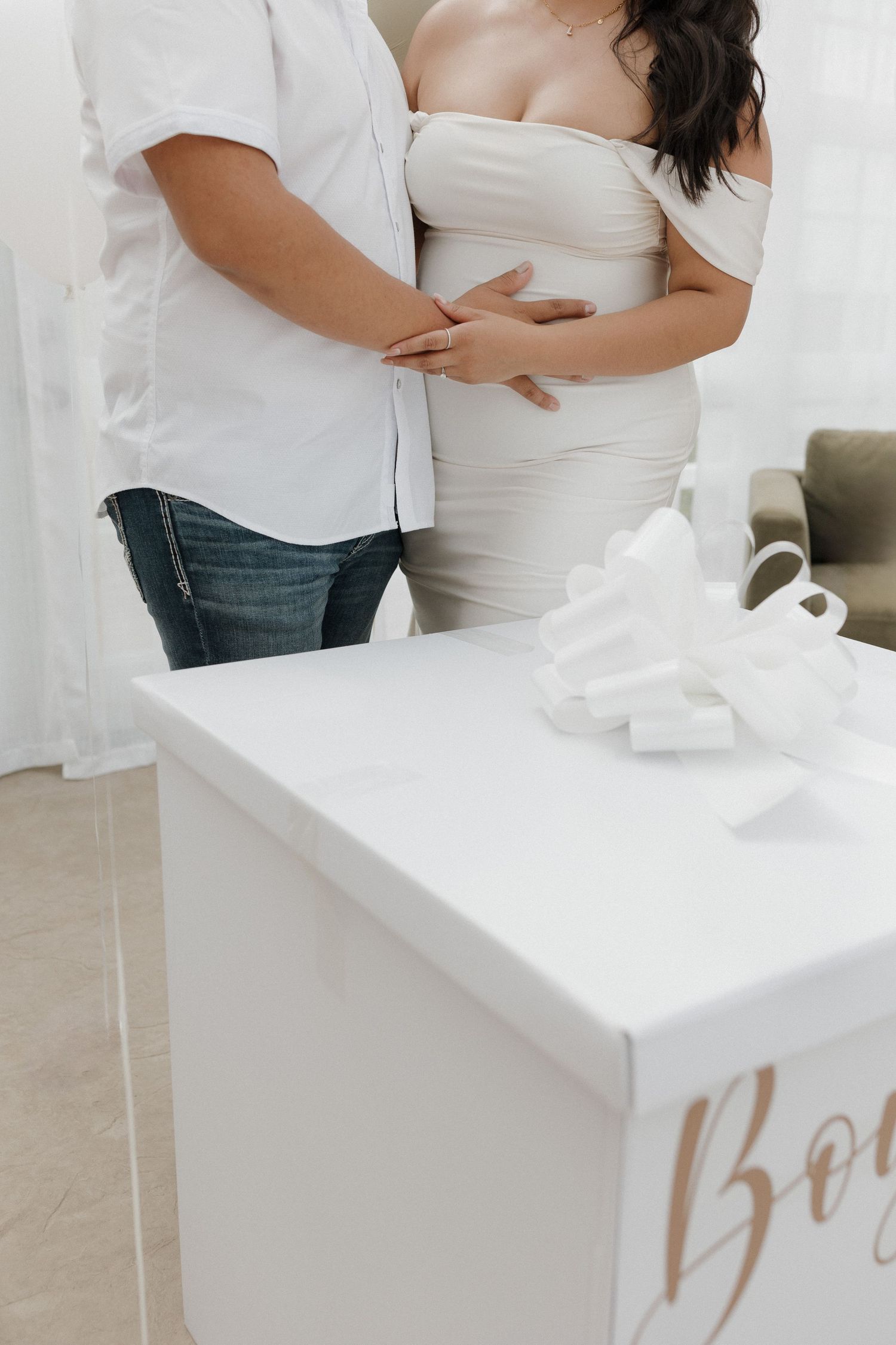 A series of white gift boxes with rose gold text sit on a white surface while someone in white touches them.