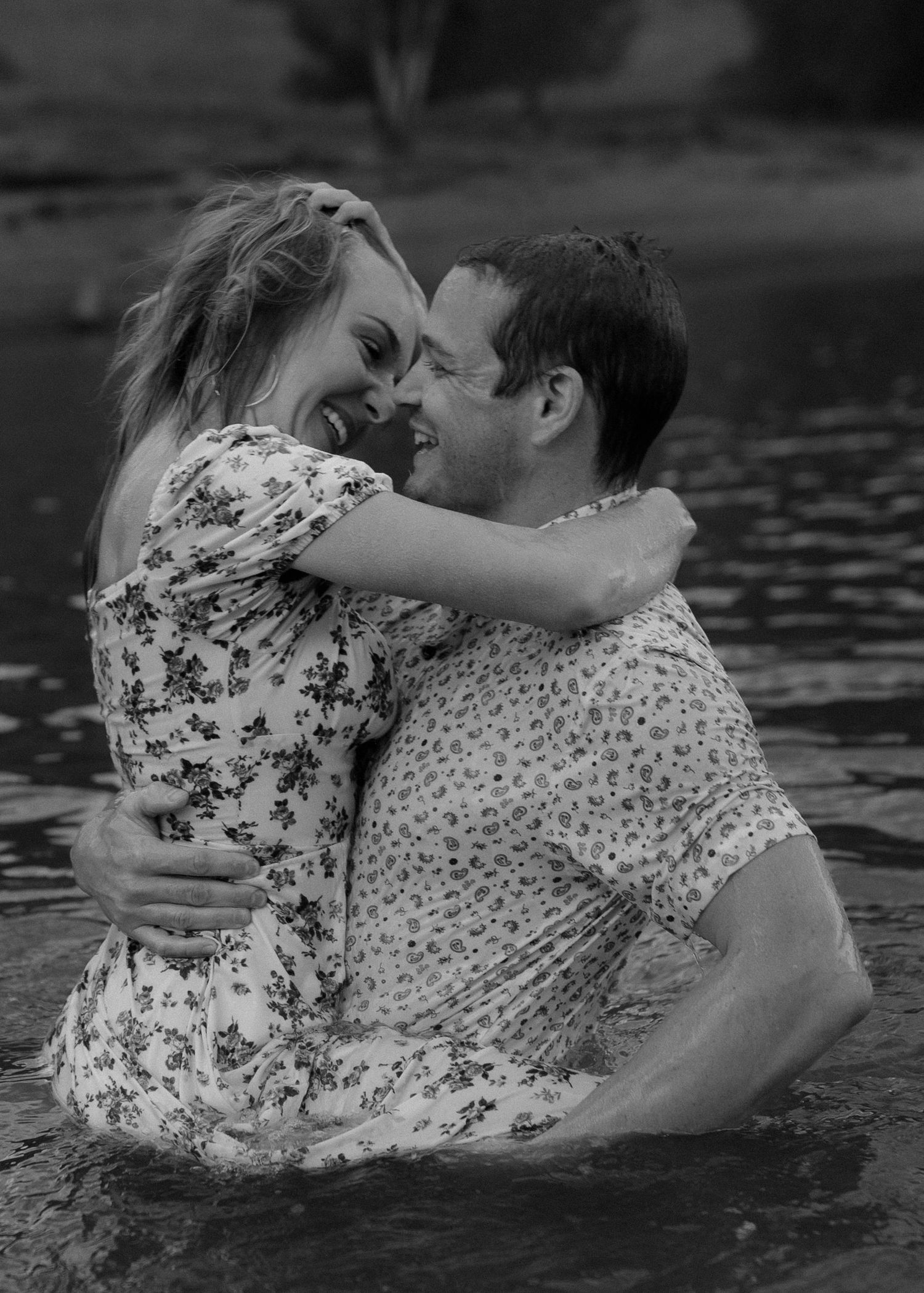 A couple embraces and kisses while floating together in dark water in a romantic black and white photo sequence.