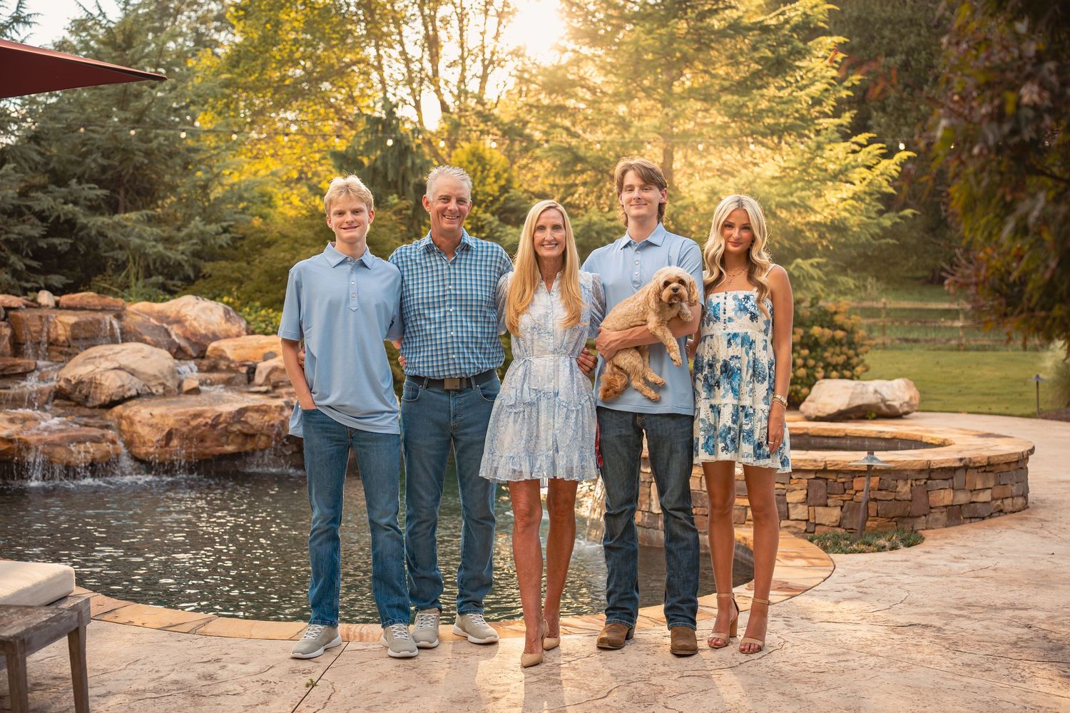 A group poses together on natural stone steps in a park during golden hour with autumn foliage in the background.