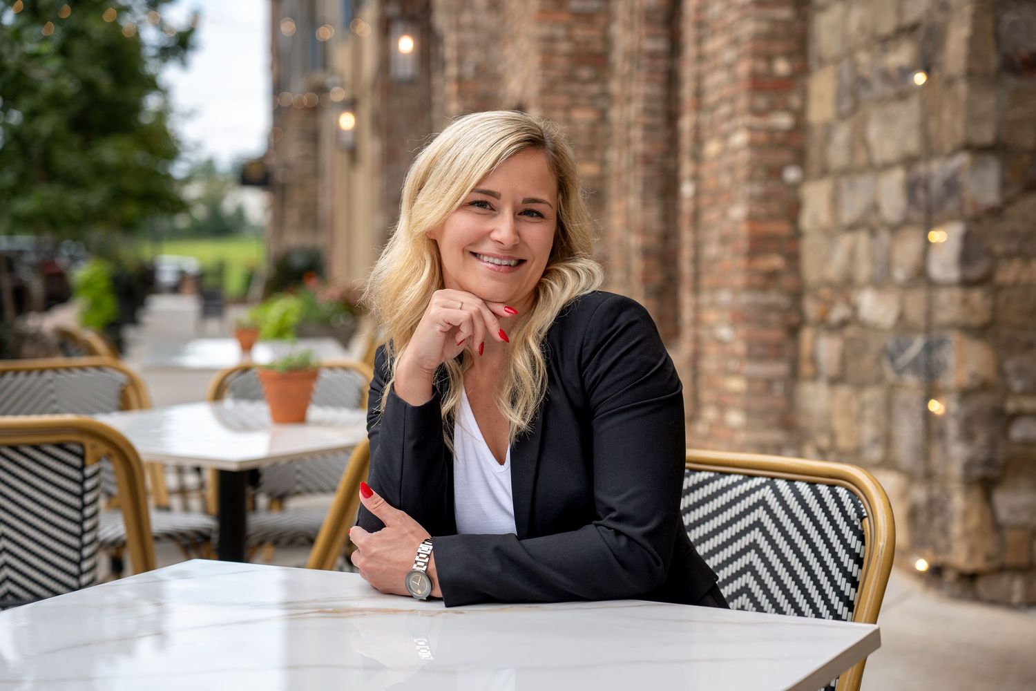 Professional sitting at outdoor cafe table with stone wall background and bistro style chairs.