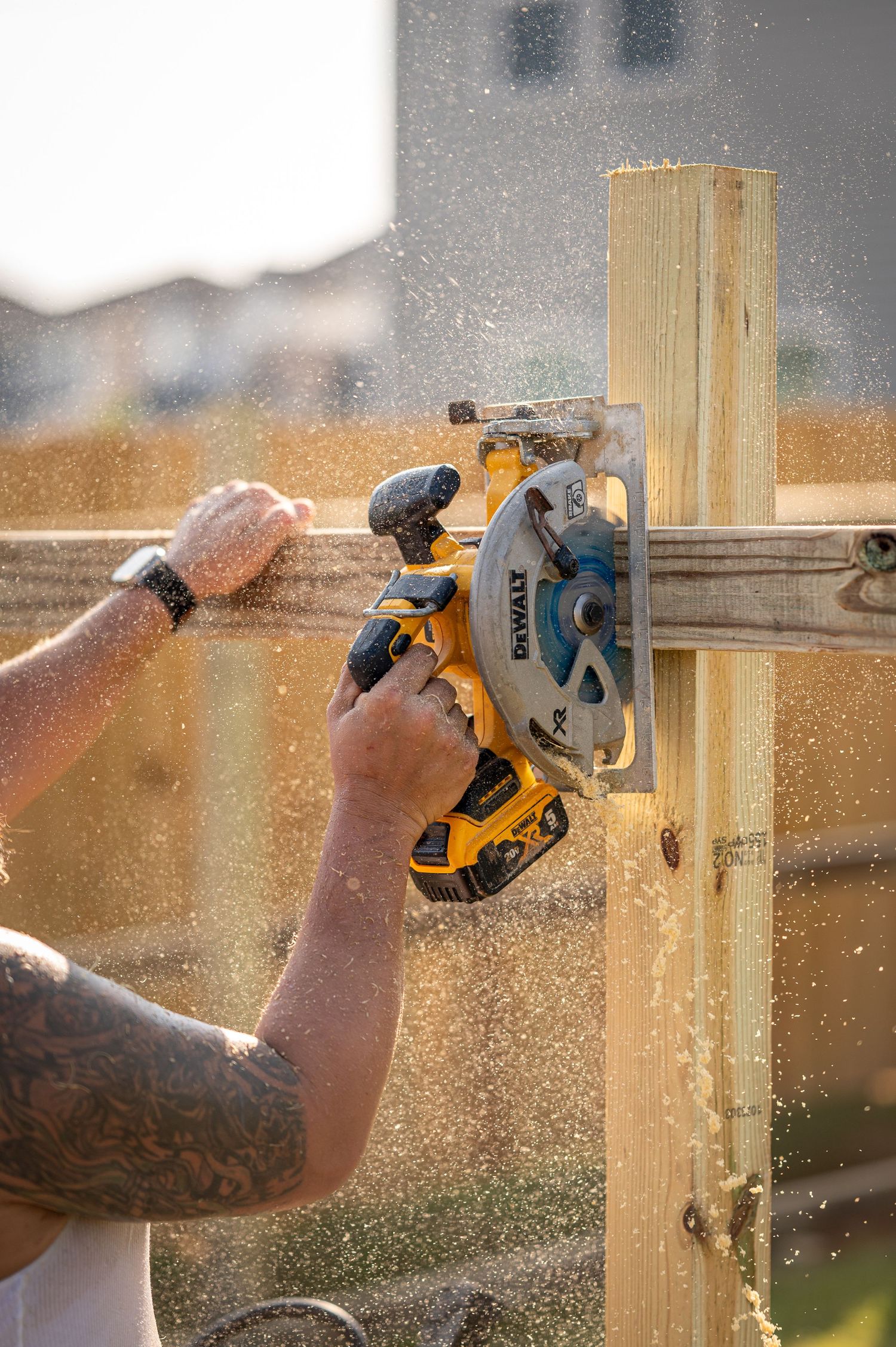 Close-up of hands using yellow power saw to cut wooden board with sawdust flying.