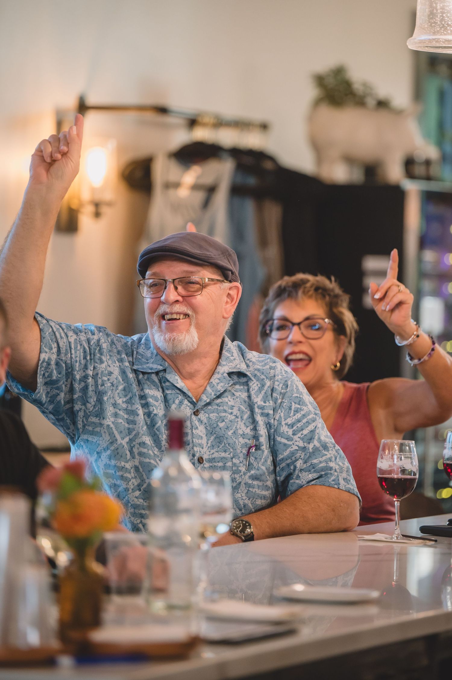 Enthusiastic people raising their hands while enjoying drinks at a restaurant bar counter.